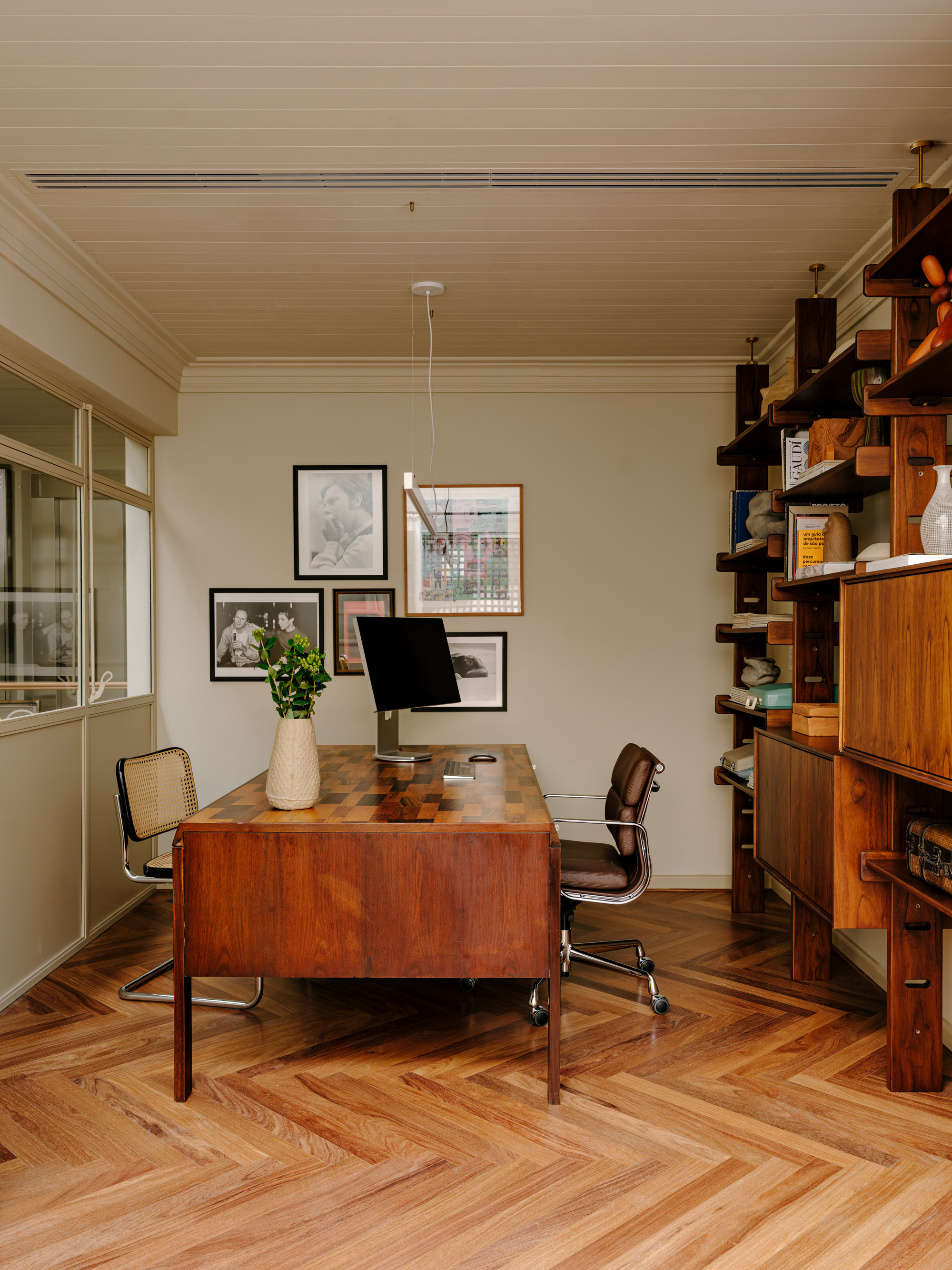 Study with a parquetry-top timber desk, leather chair and wall-mounted teak shelving on a herringbone floor
