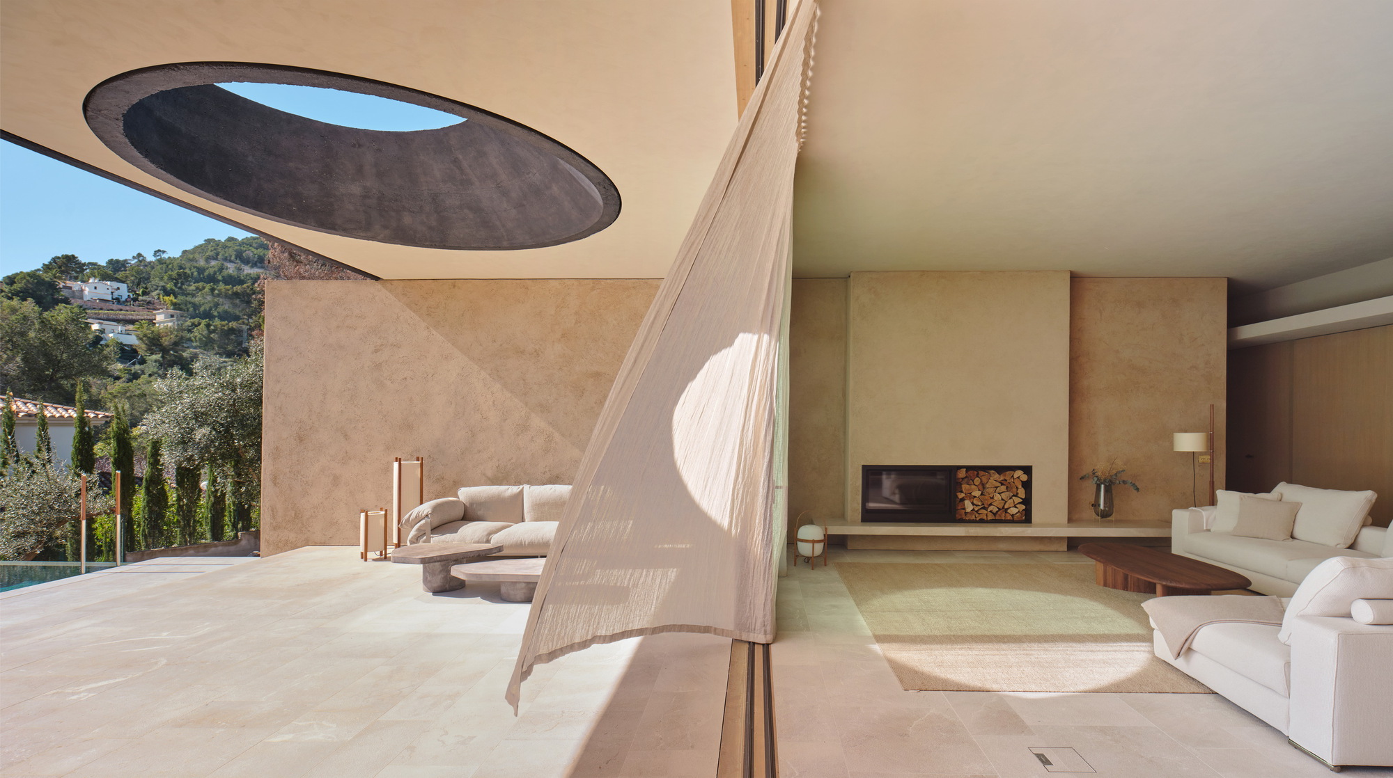 Living area opening to the terrace, with a sheer curtain blowing in front of a fireplace wall and a round roof opening