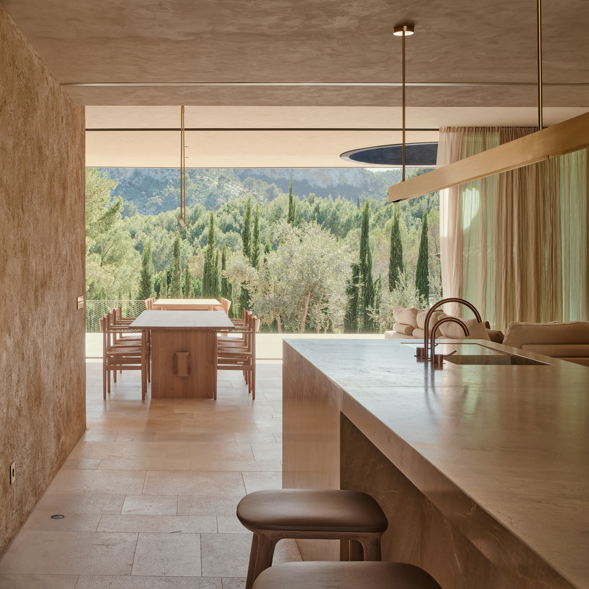 Kitchen island in veined stone facing a timber dining table, with cypress and pine hills seen through the open glazing