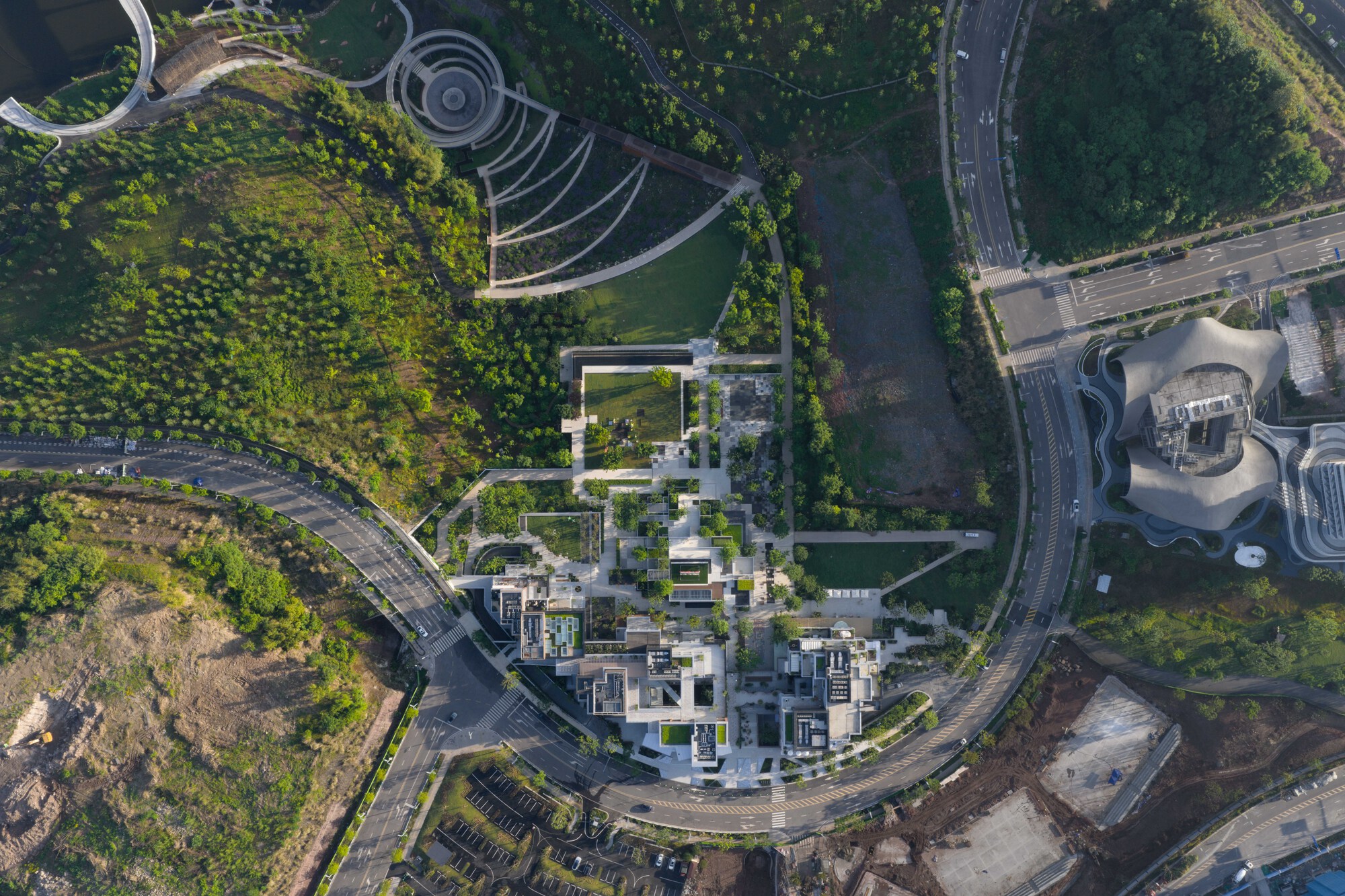 Aerial view of the terraced building cluster and garden paths wrapped by a curving road, with green hillsides on either side