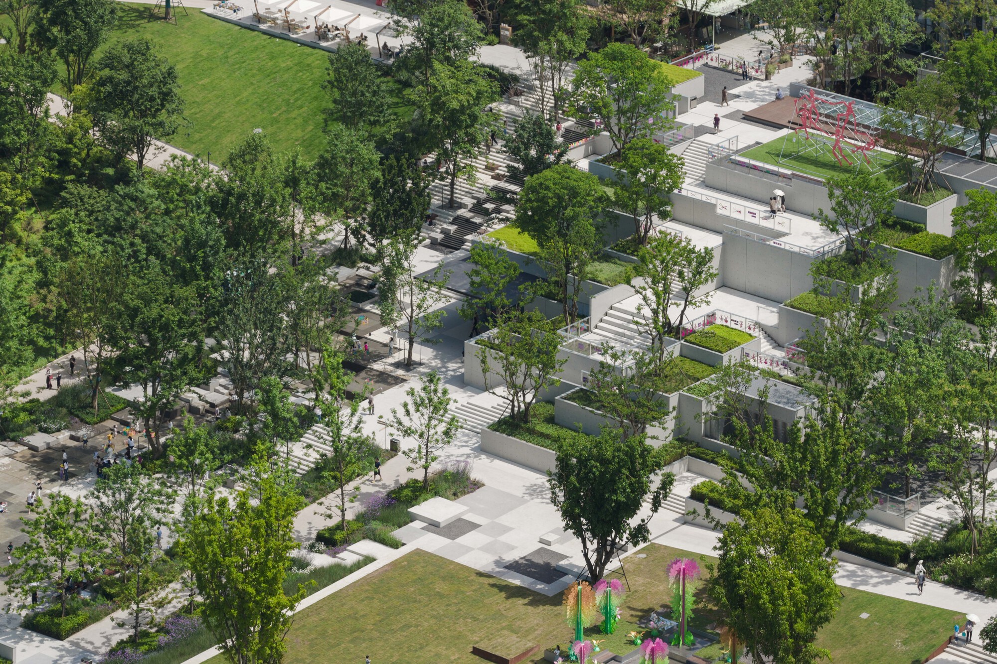 High-angle view of stepped concrete planters, staircases and lawns among trees, with visitors walking the paths in daylight