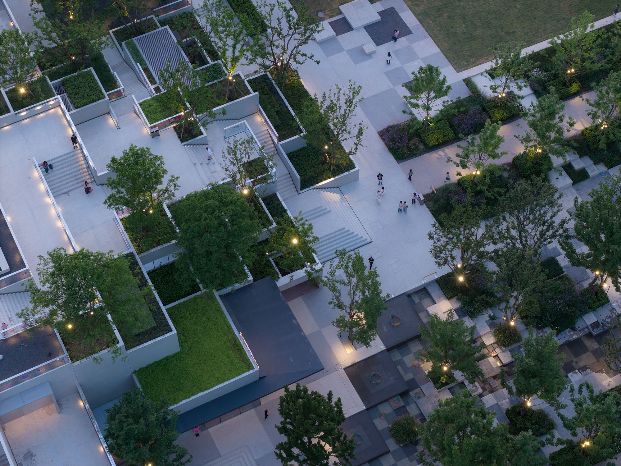 Top-down view of stepped planter terraces, staircases and checkered paving with small lights among trees at dusk