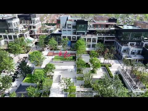 Aerial view of terraced planted courtyards and white stairs stepping between mid-rise buildings, with a red sculpture on a green lawn in daylight