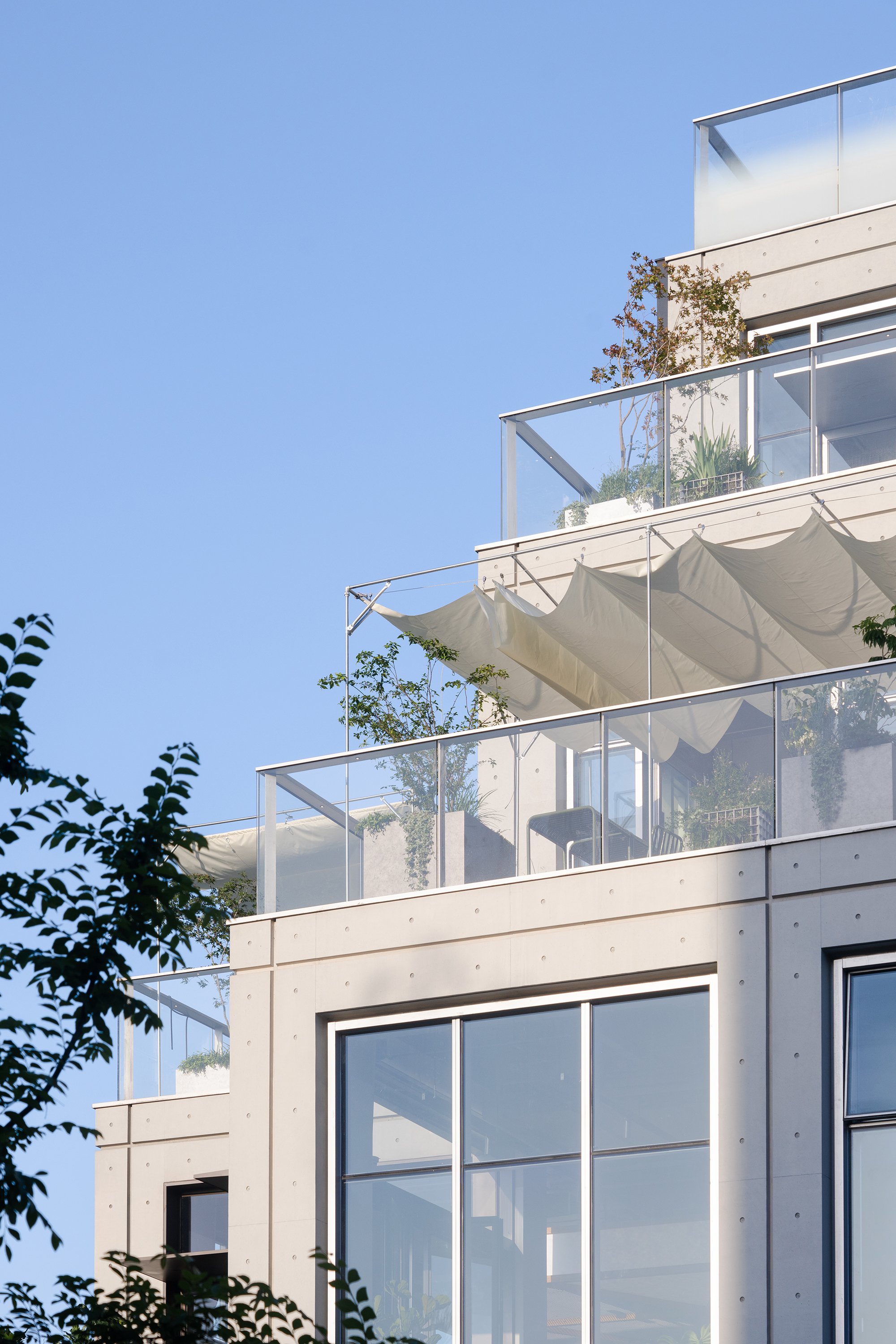 Stepped upper terraces with glass balustrades, potted plants and a rippled white fabric canopy against a deep blue sky