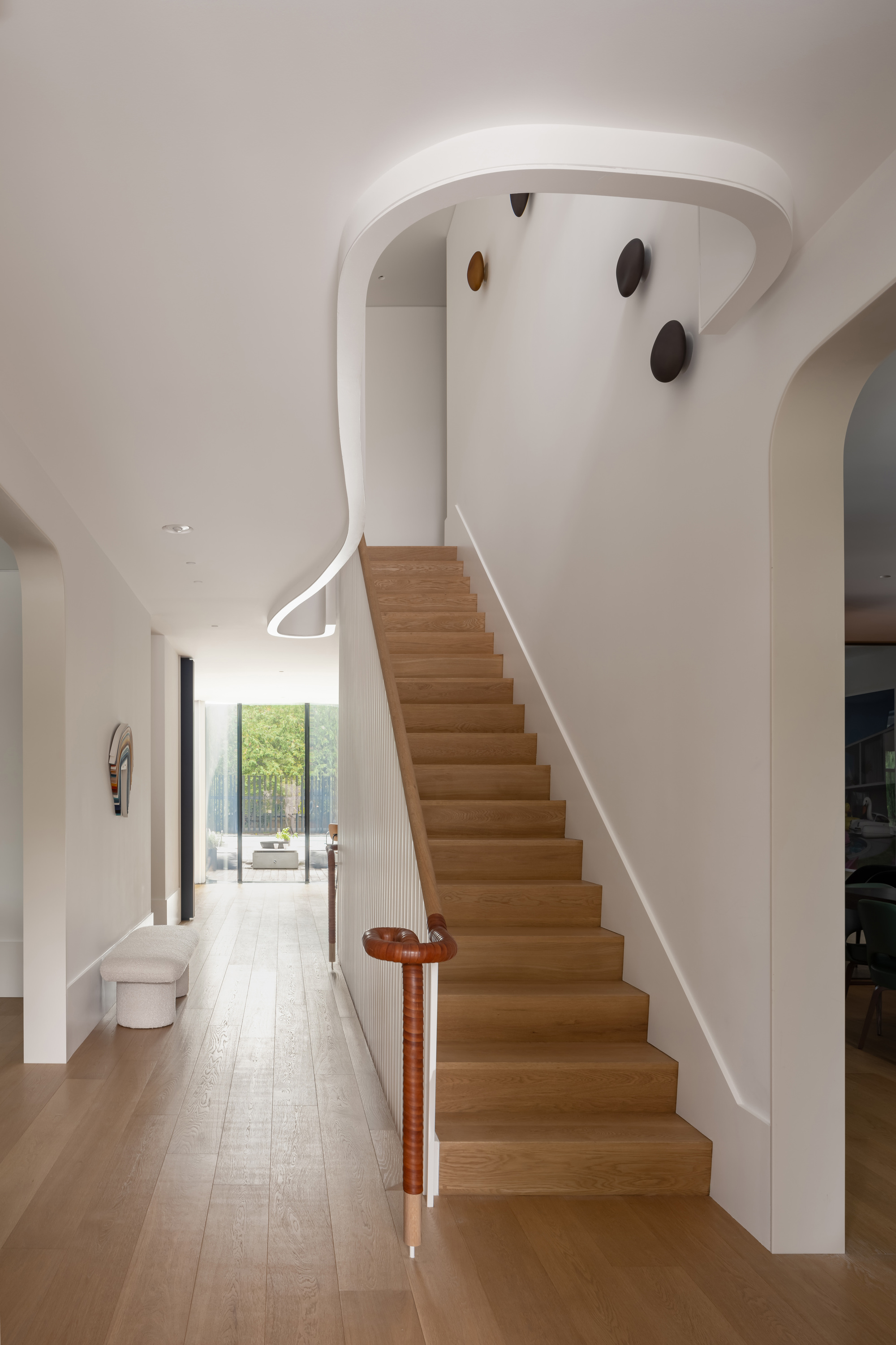 Oak staircase with a leather-wrapped newel and a looping ceiling cove, leading the eye down the hall to a glazed garden door
