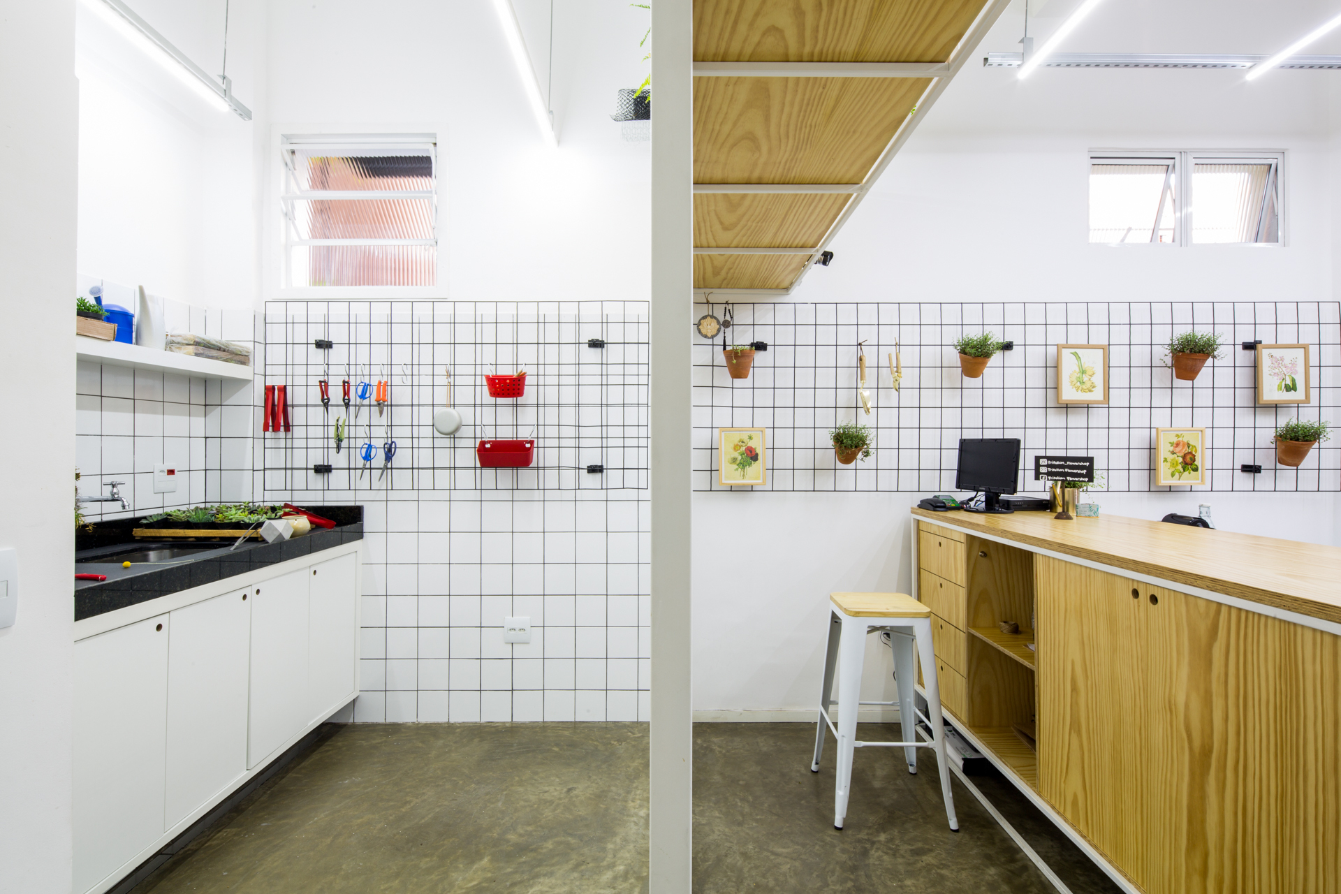 Back work area with white tile wall, black wire grid hung with tools and framed botanical prints above a plywood counter