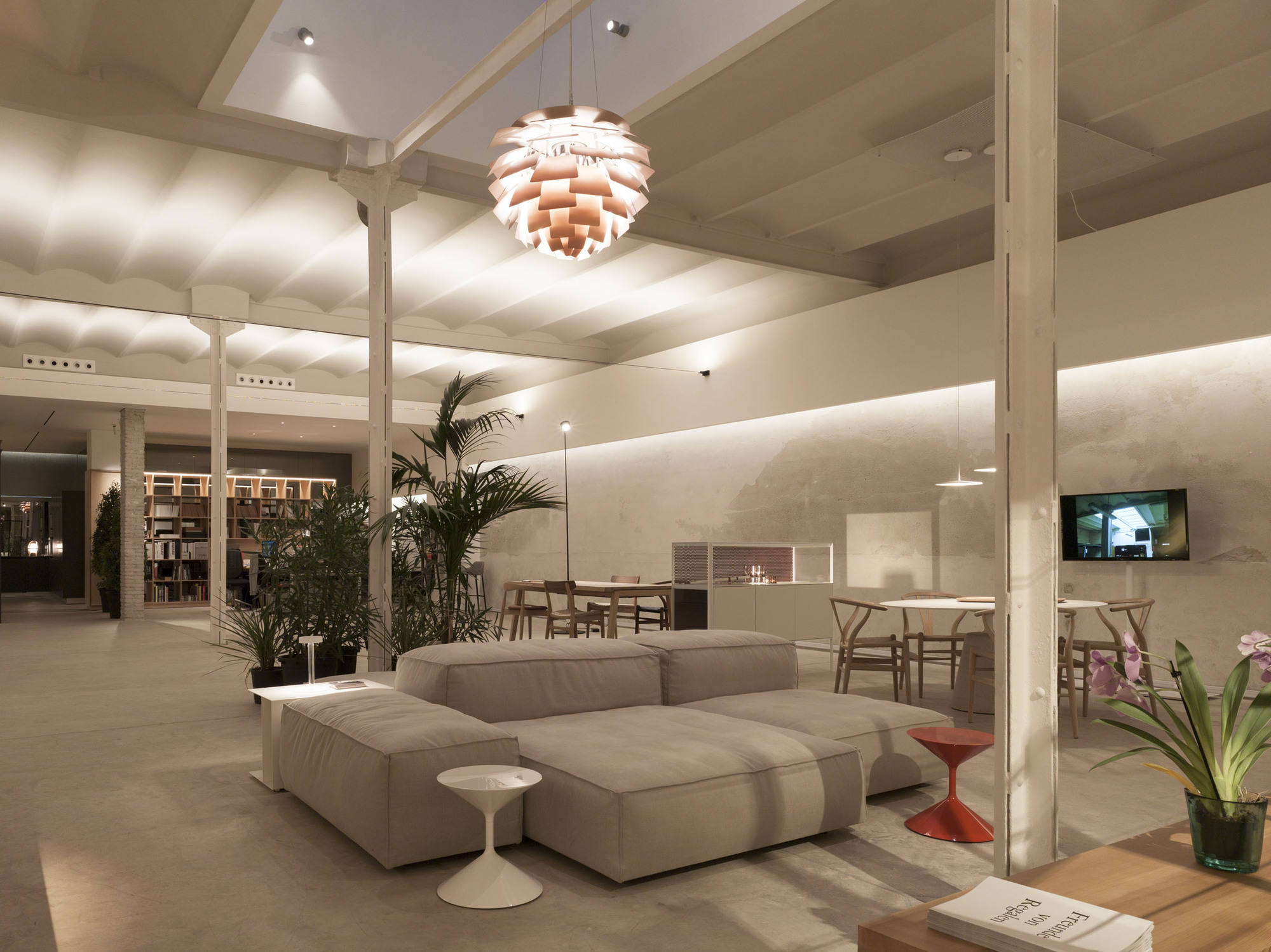 Low modular sofa beneath a copper pendant lamp, with potted palms and slim white columns under a scalloped vaulted ceiling