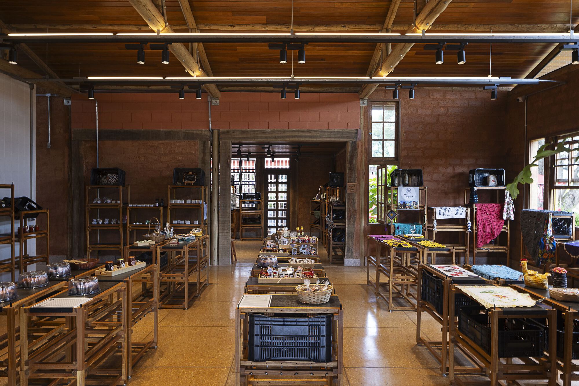 Interior market hall with wooden display tables, exposed brick walls and timber ceiling beams, daylight coming through windows and a rear doorway