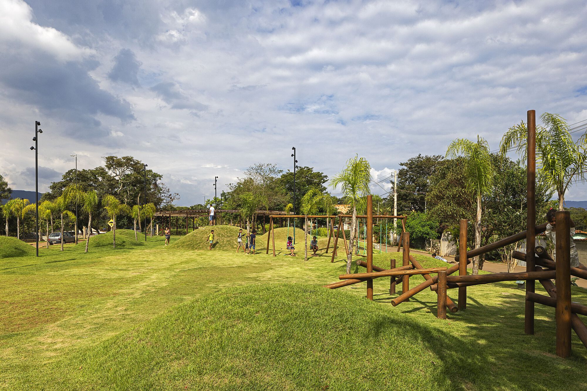 Low view of grass mounds, a timber swing frame and log play structure in afternoon sun