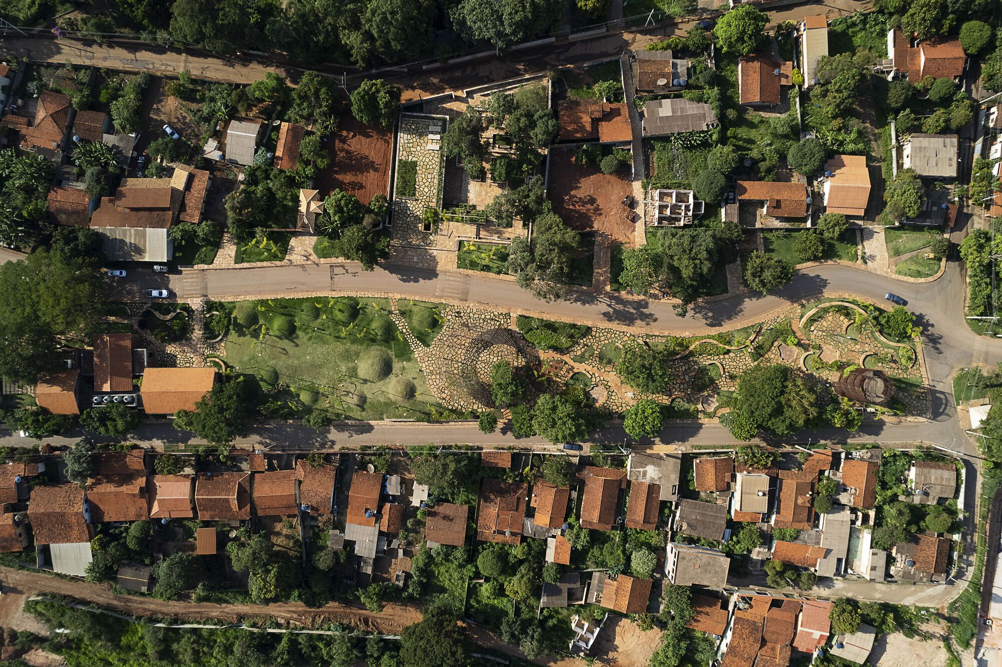 Aerial view of a street-side garden with a circular stone-paved pattern and grassy mounds among tiled-roof houses in low sun