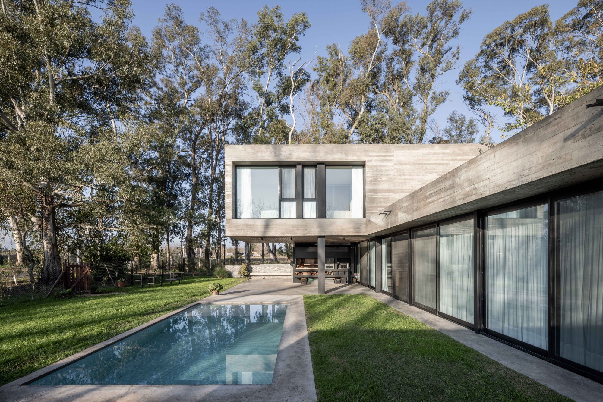 Pool and lawn beside the glazed ground floor, with the cantilevered concrete box above and tall eucalyptus trees behind