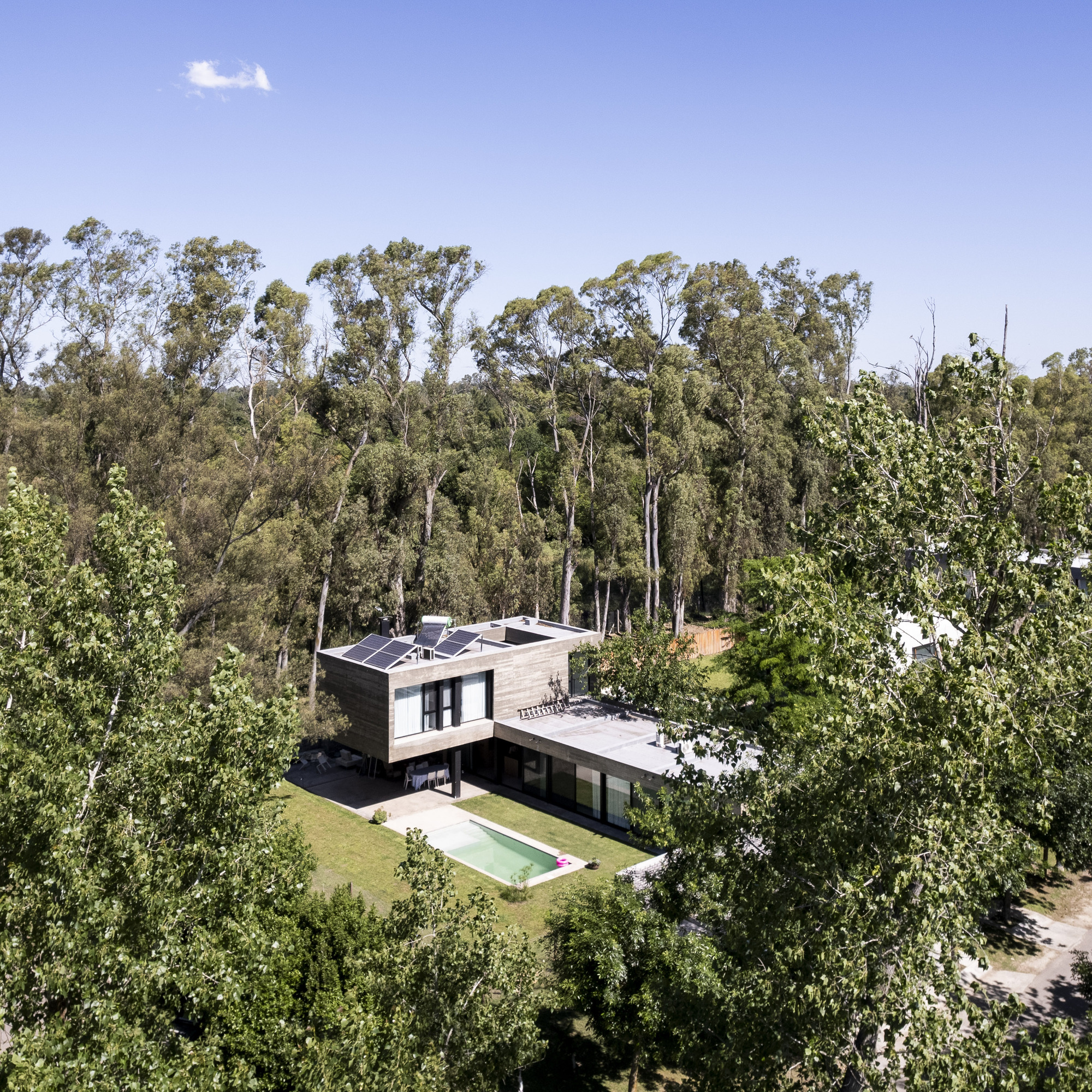 Aerial view of a two-storey timber and concrete house with rooftop solar panels and a pool among eucalyptus trees