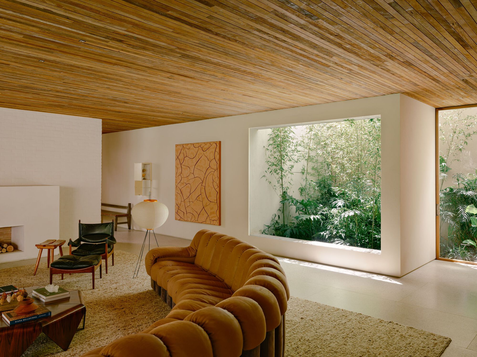 Living room with a channeled tan sofa facing a large framed window onto a bamboo planted light well