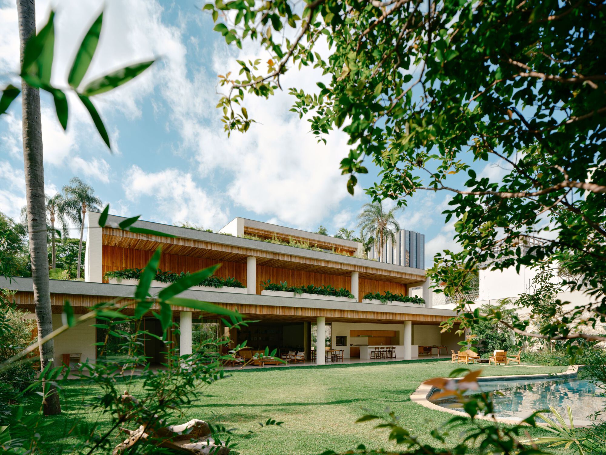 Garden view of the stepped timber-soffit house with planter boxes, a curved pool and palms under a partly cloudy sky