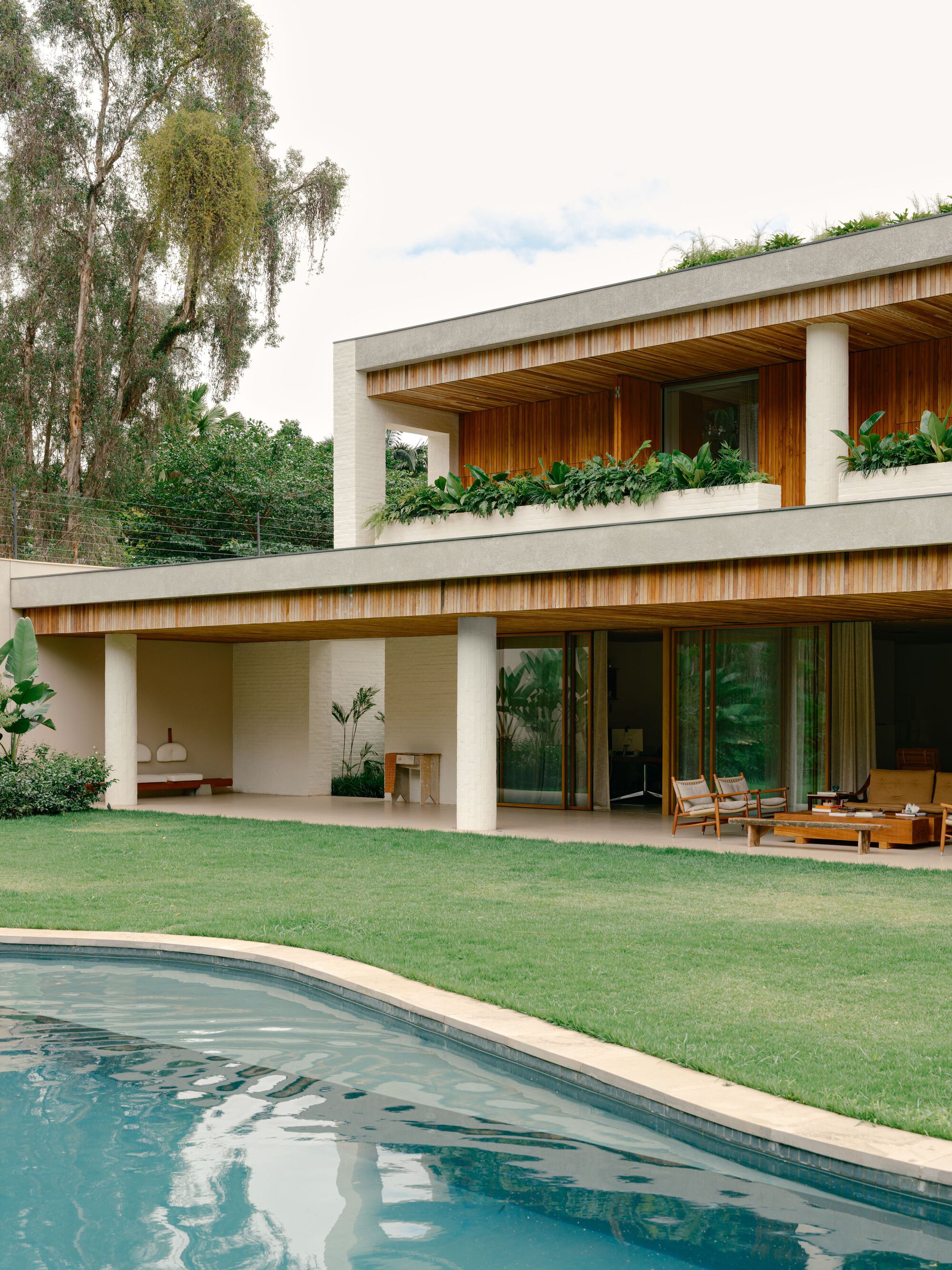Curved pool edge in the foreground with the covered porch, round columns and planter boxes behind a green lawn