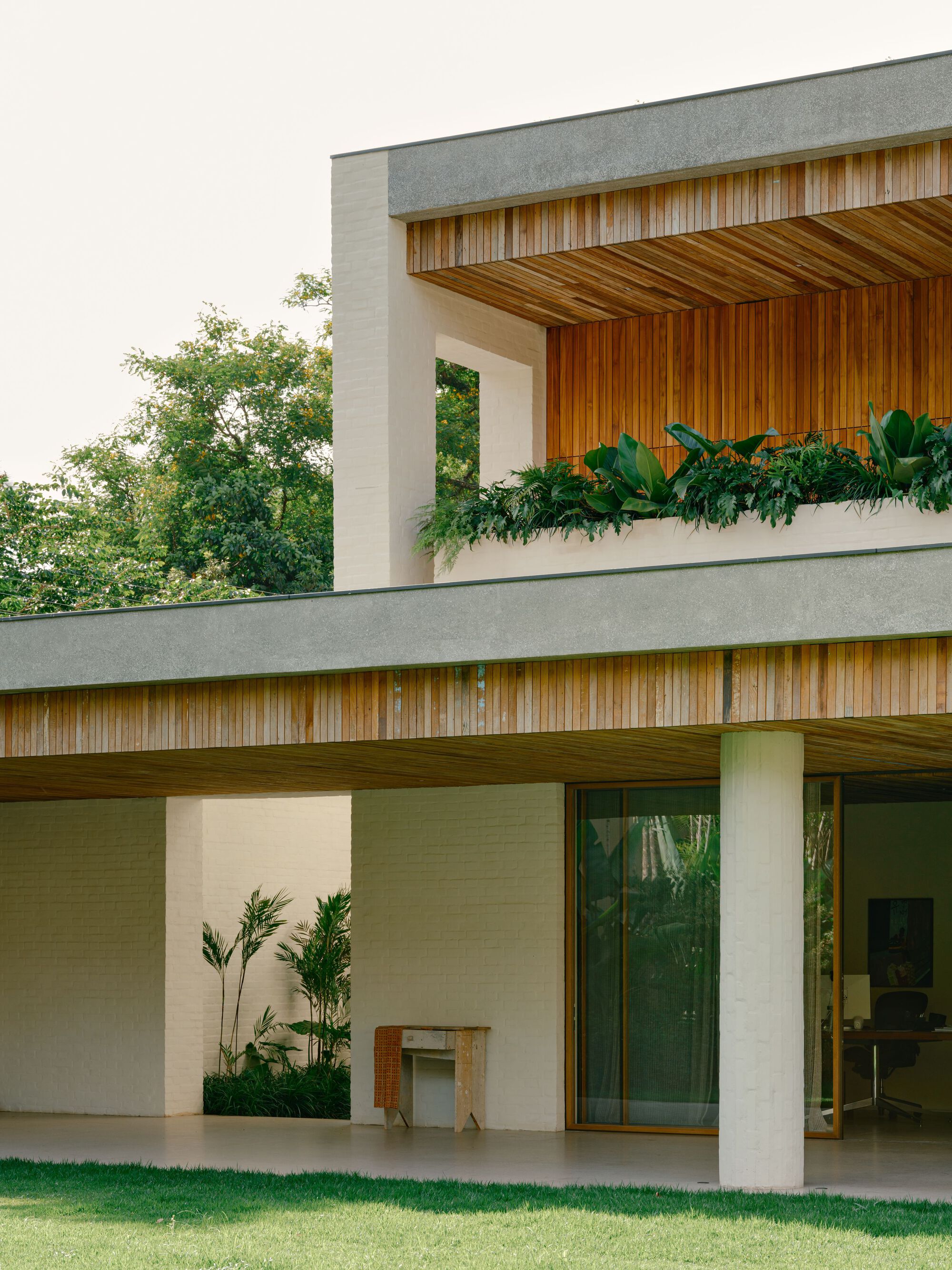 Corner detail of white brick walls, a thin concrete roof edge and cedar slat soffit above a sliding glass door