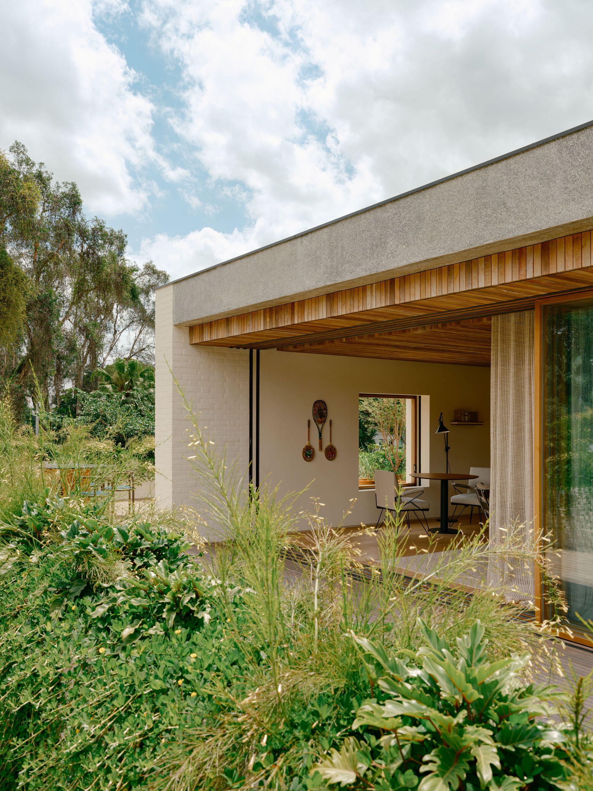 Upper-level room opening to a roof terrace of tall grasses, with a wood-framed glass door and cedar slat eave under cloud