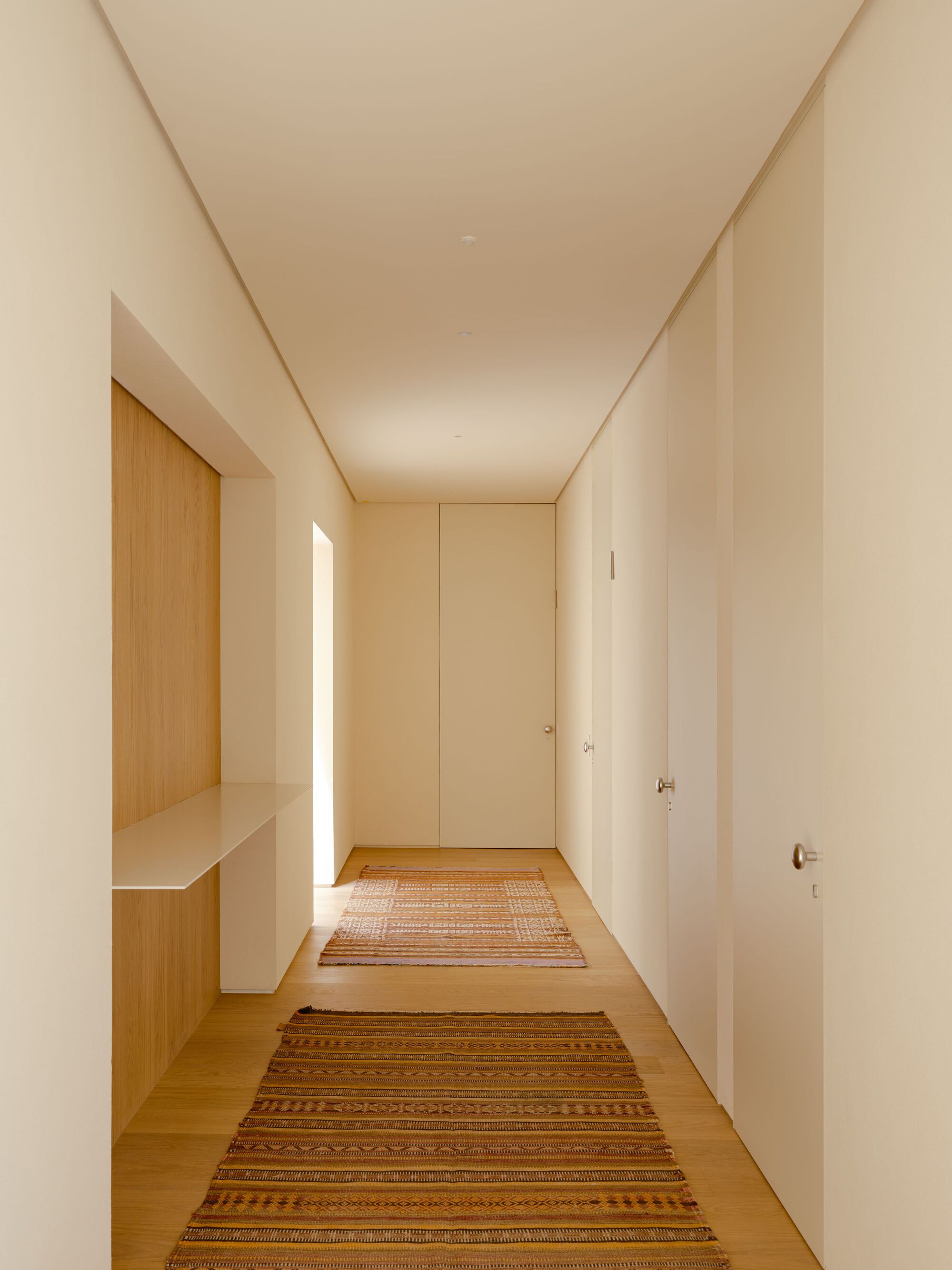 Narrow hallway with flush cream doors, an oak wall niche with a shelf, and two striped kilim runners on the wood floor