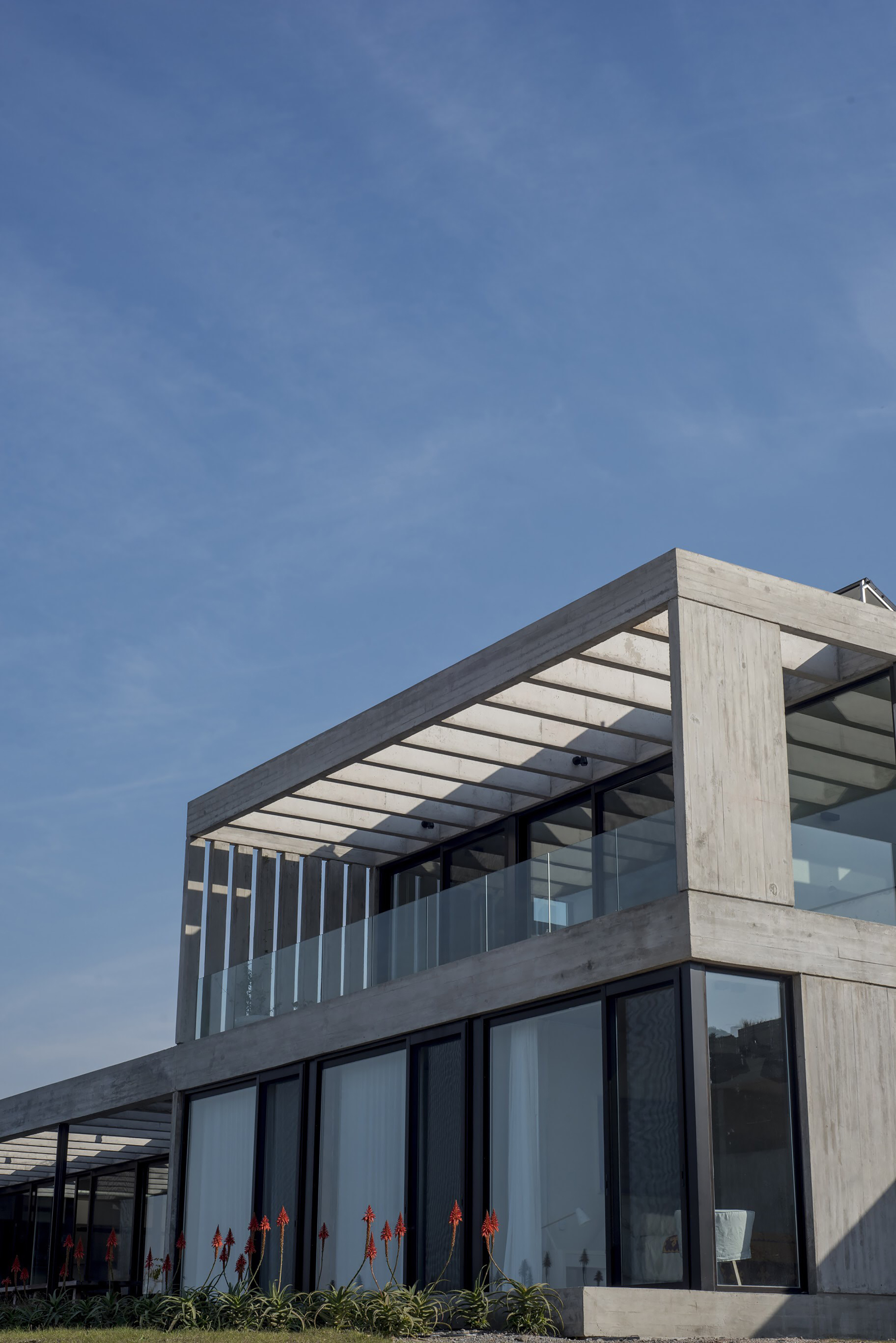 Corner of the concrete frame with a pergola of beams above a glass balustrade, red aloe flowers in the foreground
