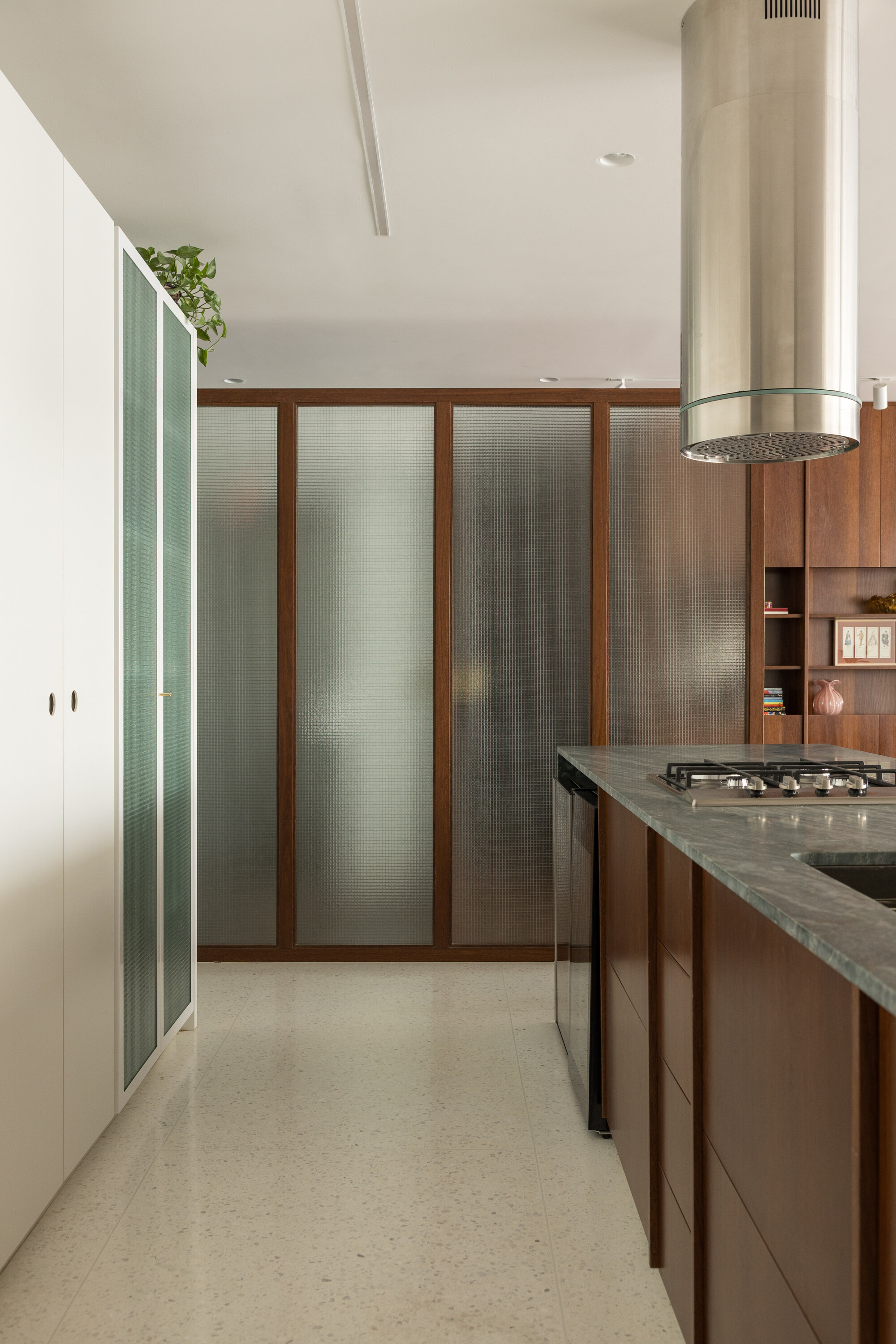 Ribbed glass panels framed in walnut beside a steel range hood, marble counter and terrazzo floor in soft daylight