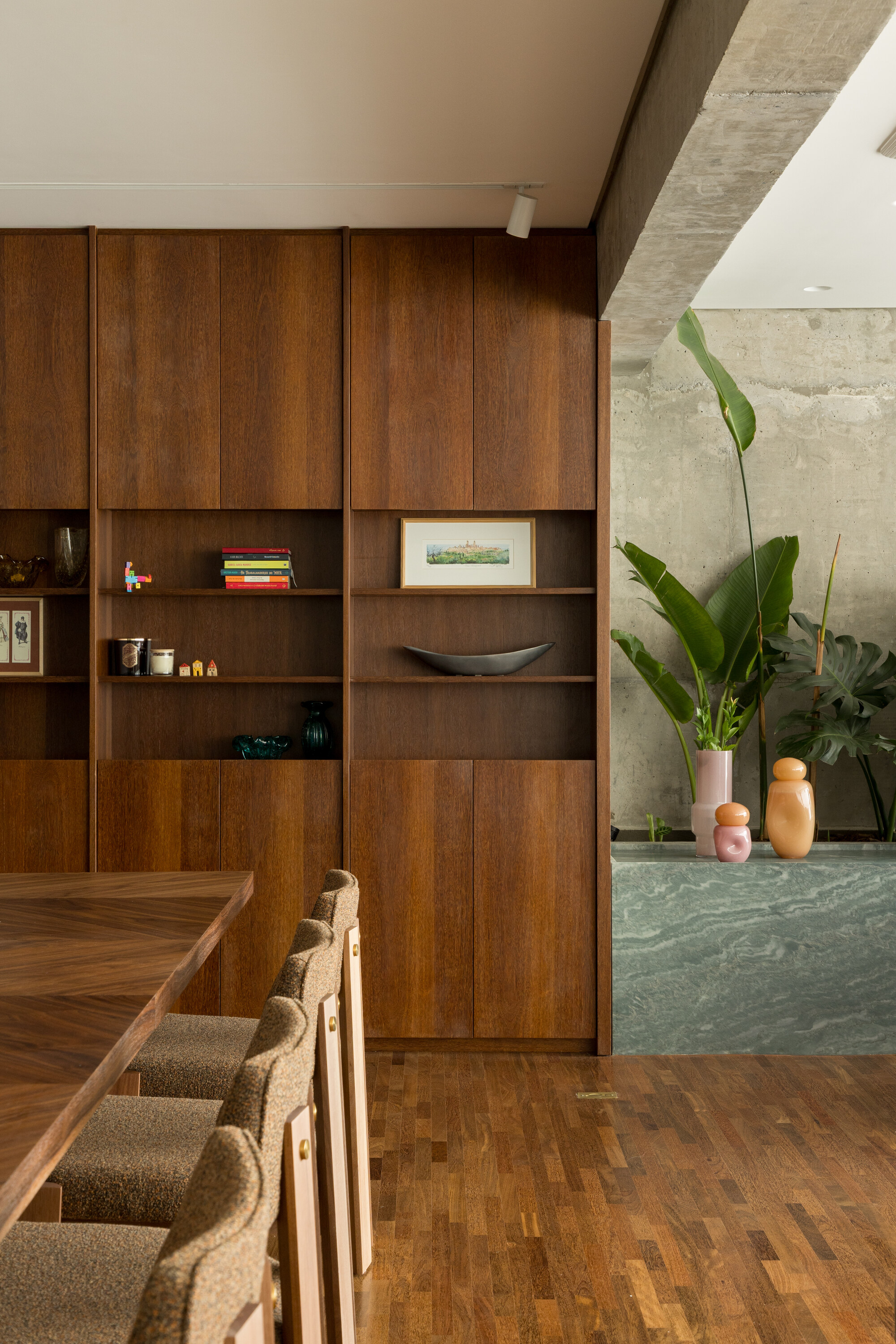 Close view of walnut cabinet doors and open shelves beside a concrete wall, banana plants and a marble planter ledge