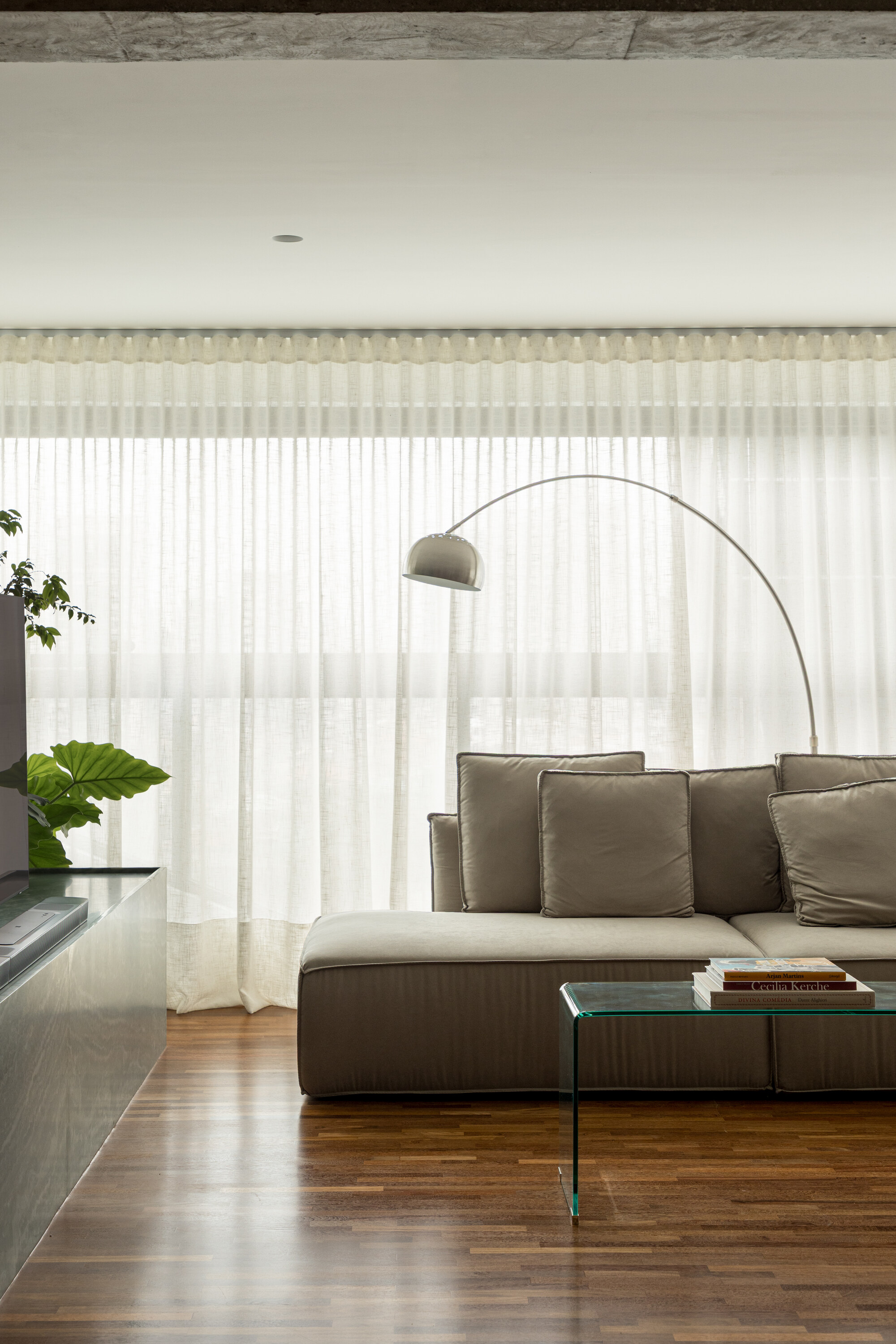 Low taupe sofa and arched floor lamp in front of floor-to-ceiling sheer curtains, with a glass side table in soft daylight