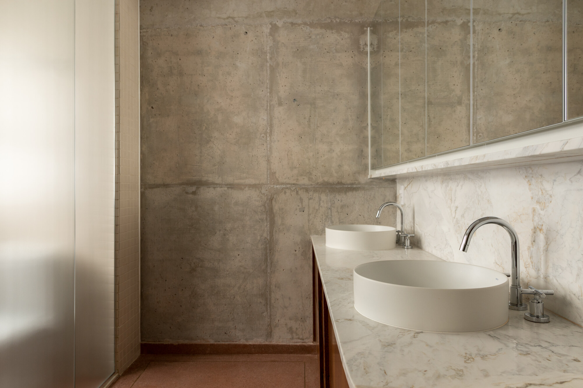Bathroom with two white oval basins on a marble counter against a board-marked concrete wall and a mirrored cabinet