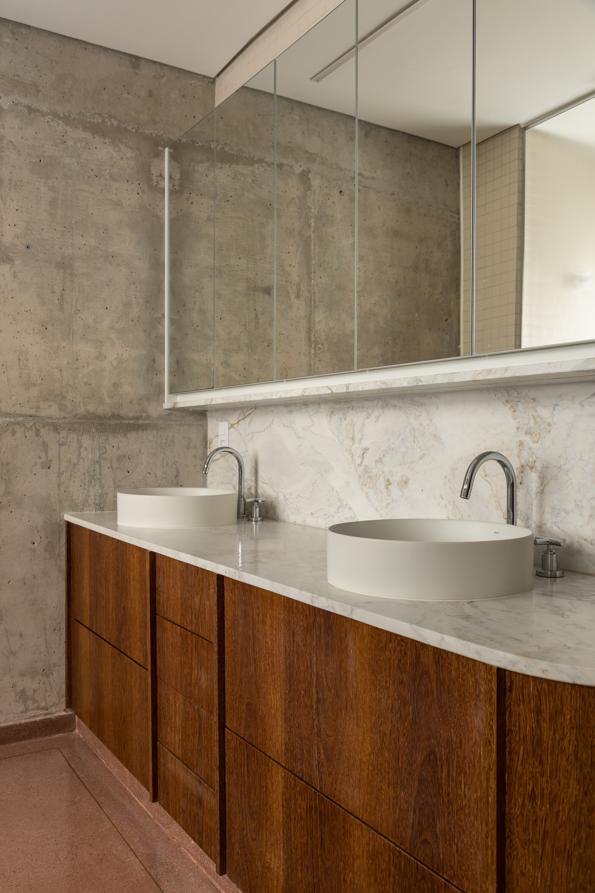 Double vanity with round white basins, a marble top and walnut drawers against a board-marked concrete wall