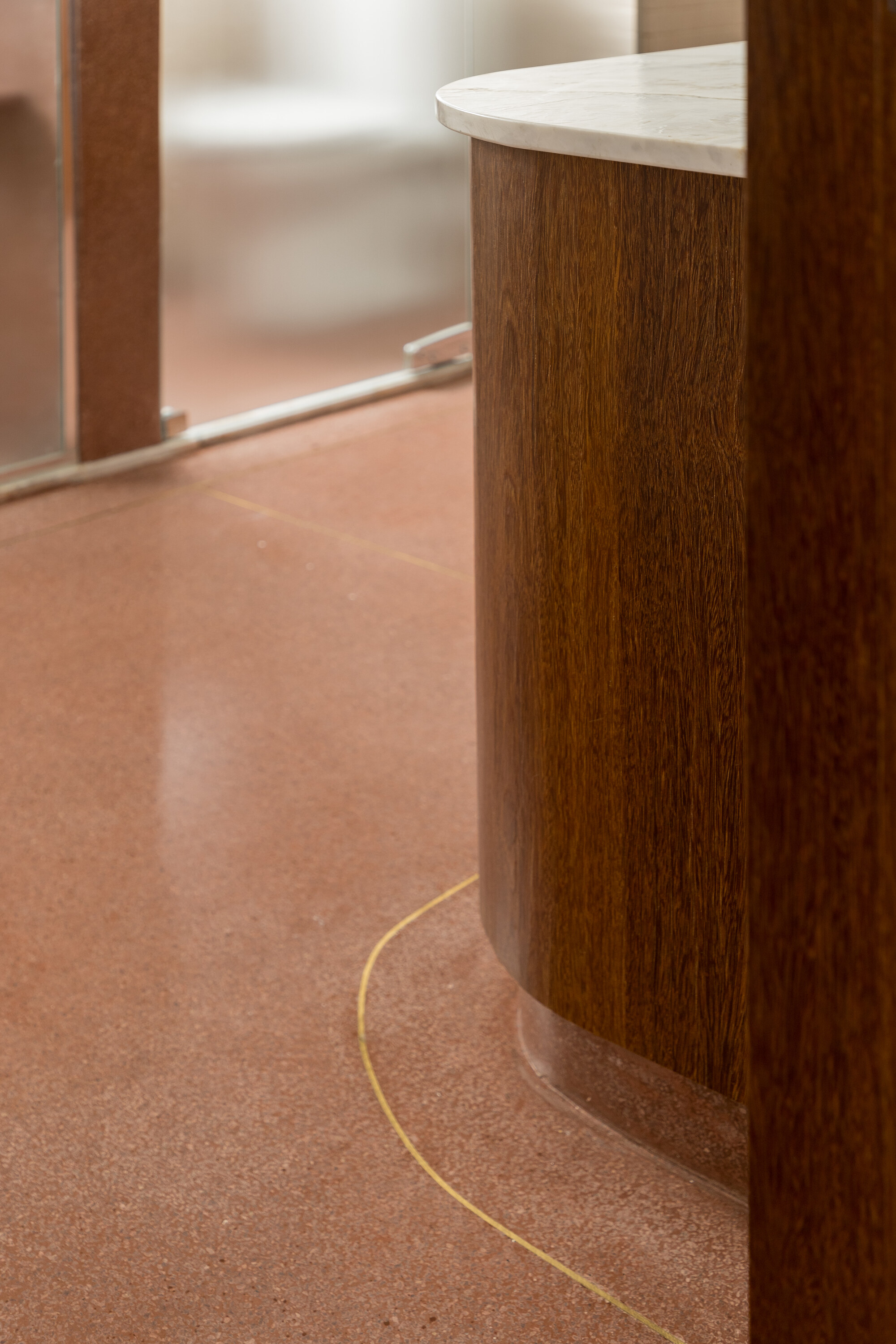Close-up of the curved timber vanity base meeting a pink terrazzo floor with a thin brass inlay line