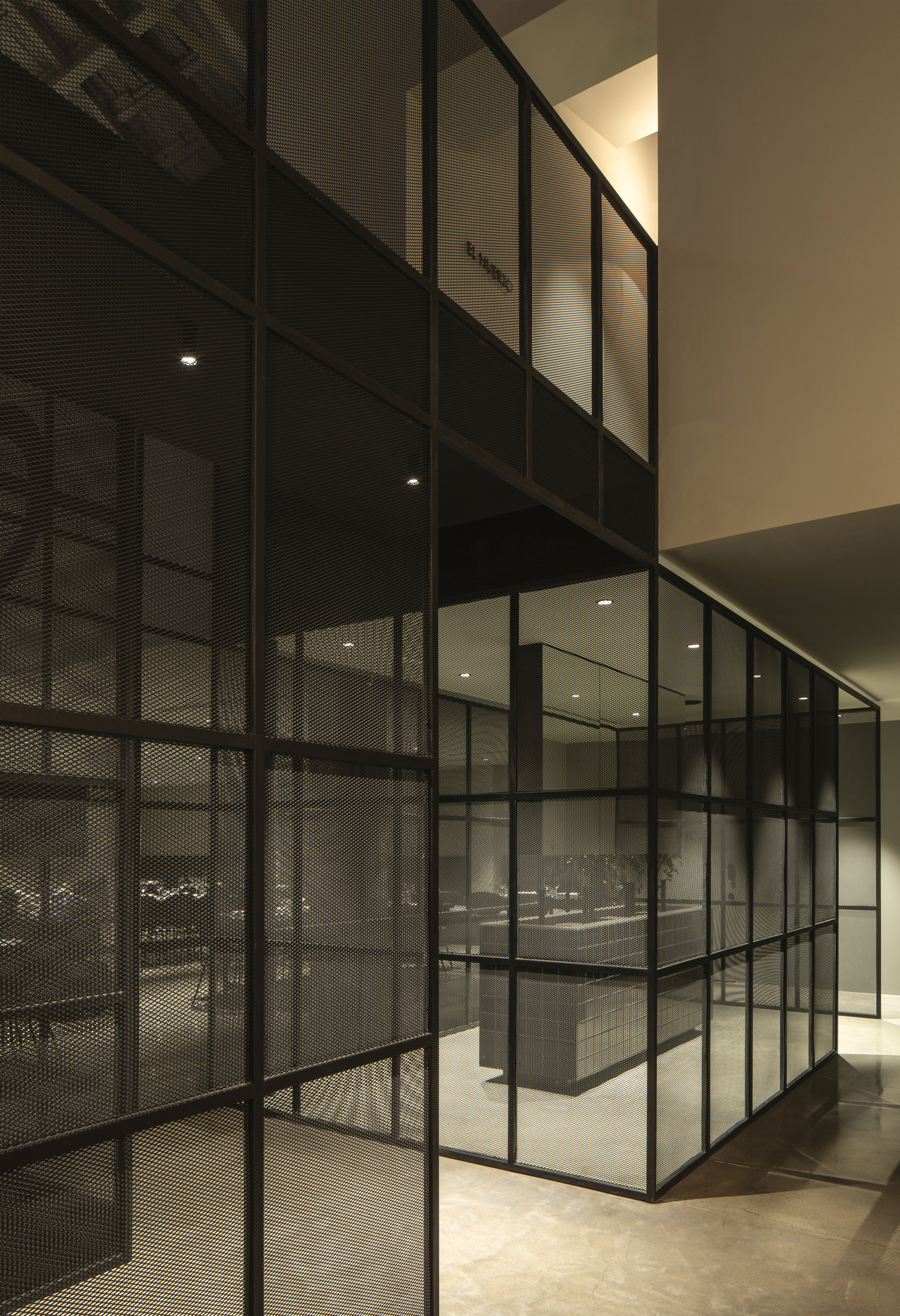 Black steel-framed mesh and glass partitions enclosing a tiled counter, lit by recessed ceiling downlights at night