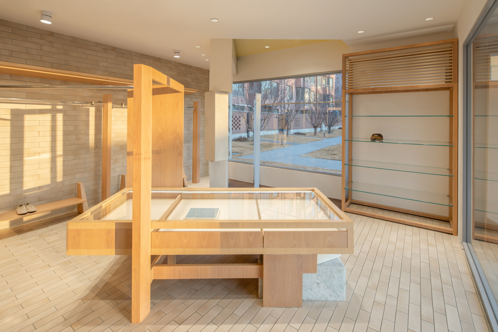 Timber display table with glass top and stone base, set before a corner window in low winter sun