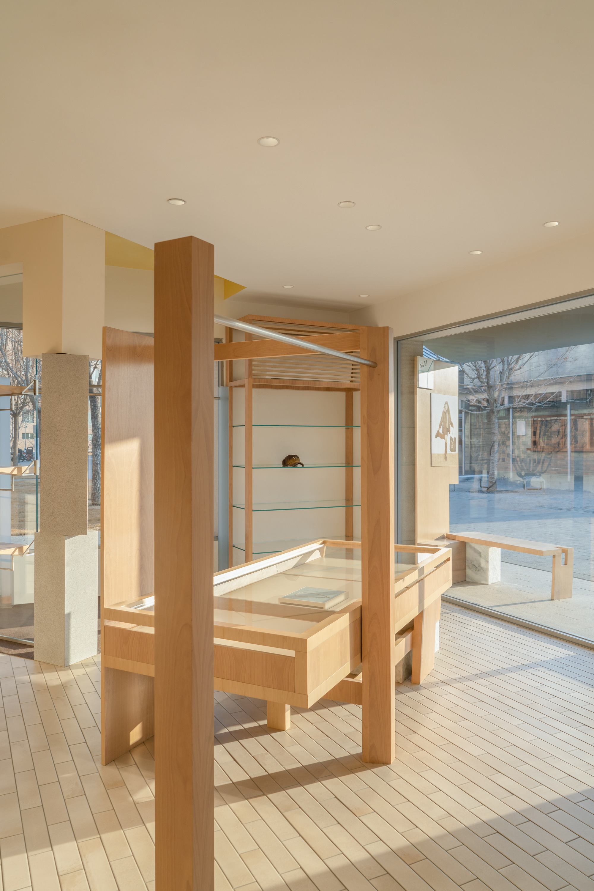 Vertical timber posts and a glass-topped display case on a strip-tiled floor, lit by low sun through the window wall