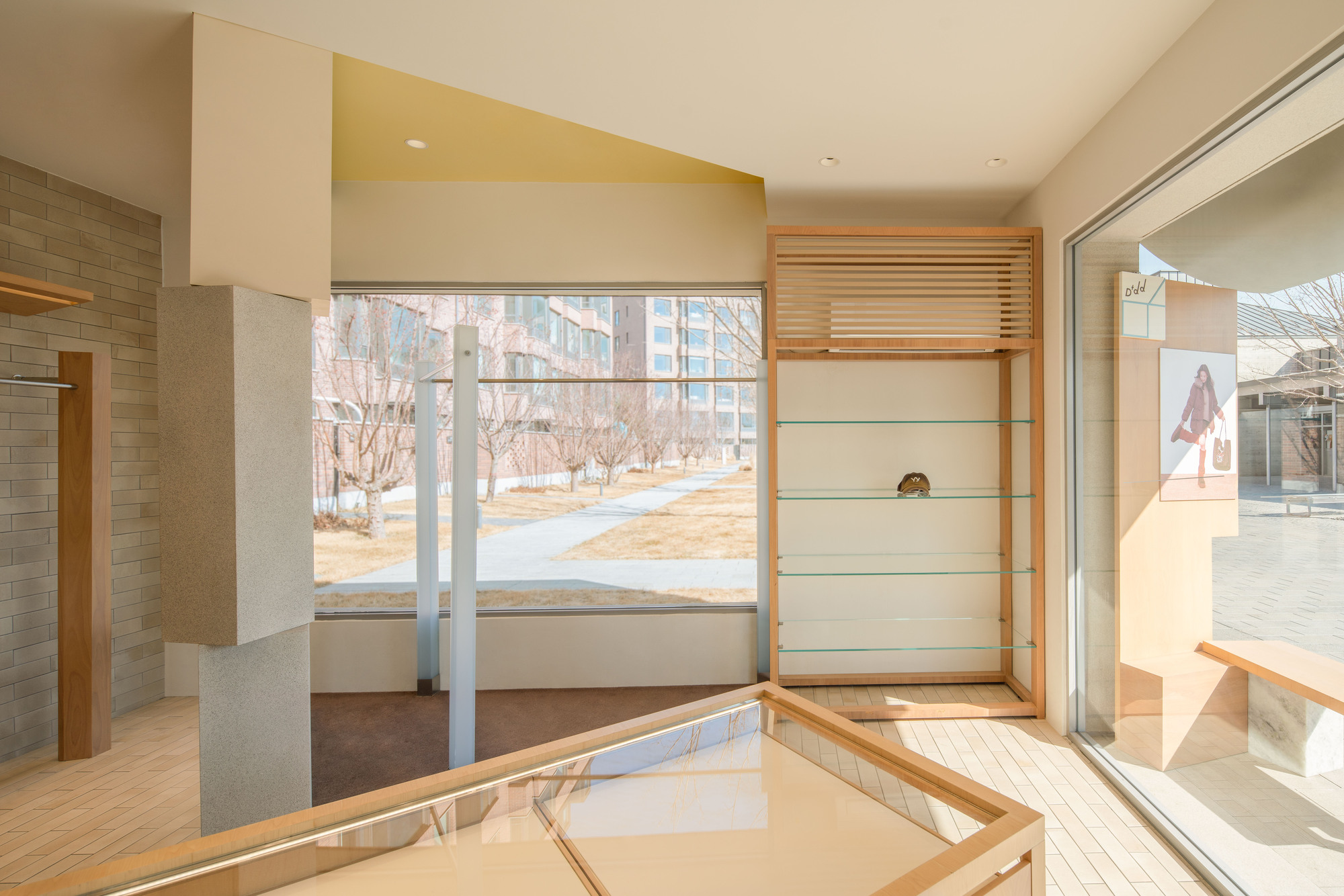 Glass-shelved timber cabinet and stone-clad column facing a window onto a garden path with bare winter trees