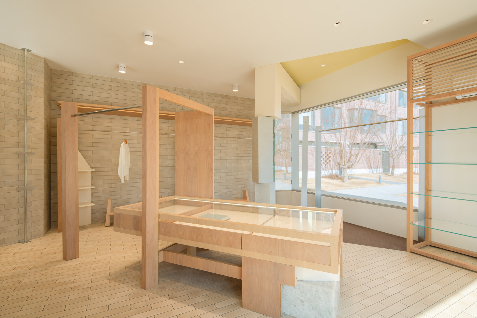 Timber frame and display table in front of a brick-tiled wall with a hanging white robe, yellow ceiling plane above