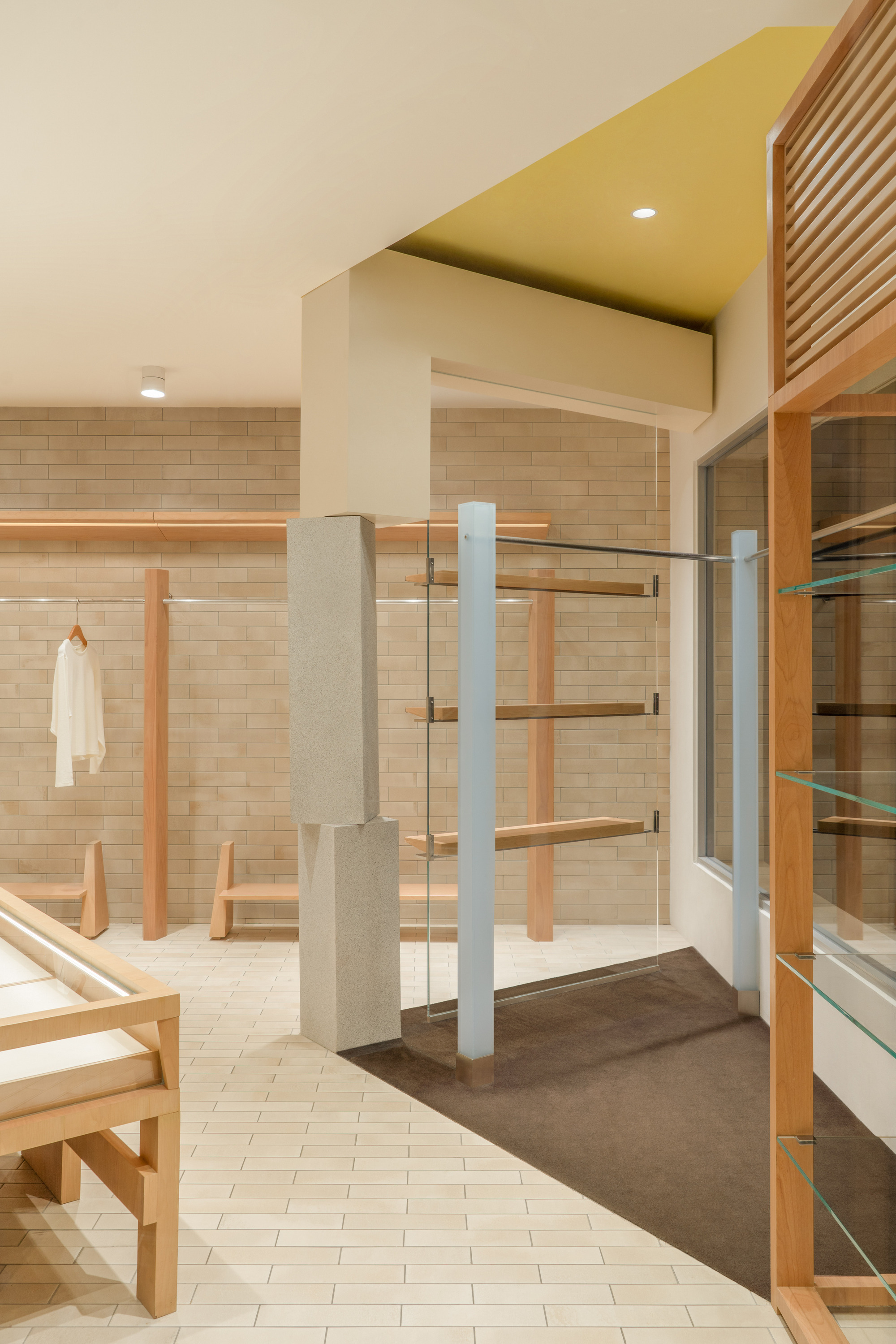 Retail floor with a stone-clad column, glass shelving panel and yellow ceiling recess over a dark carpet inset