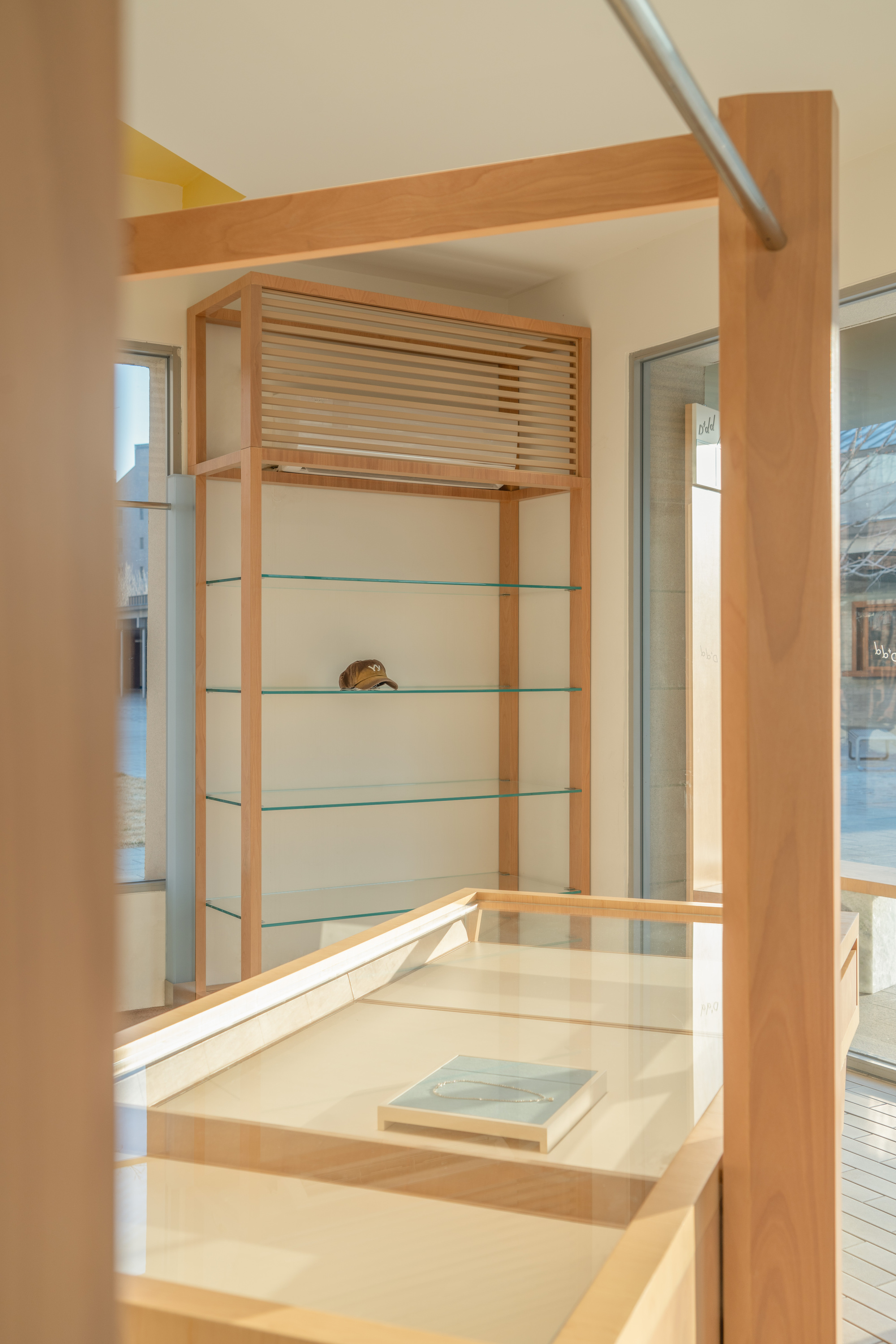 Timber-framed glass shelving unit holding a cap, seen past a display case with a book in low sun