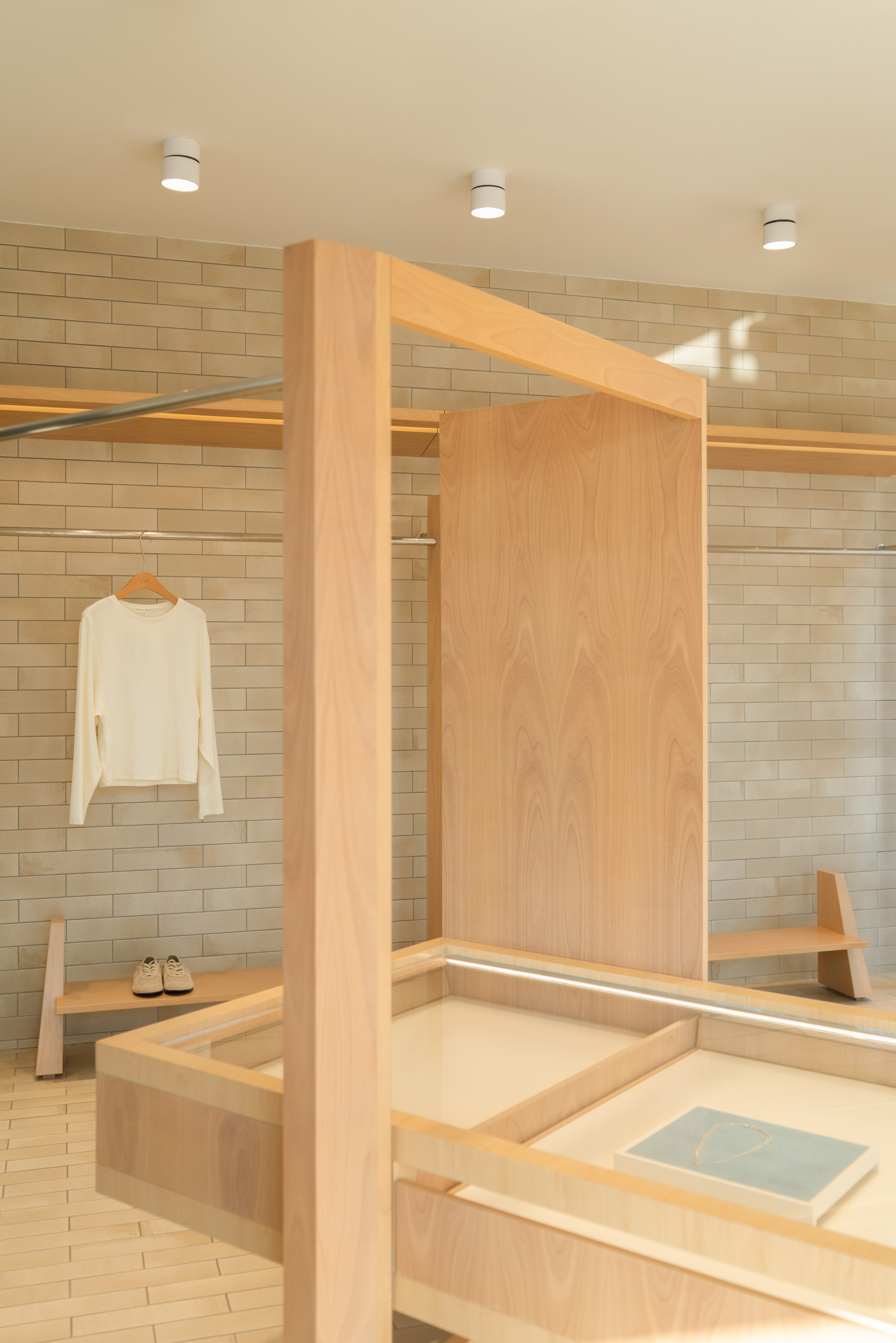 Timber portal frame and veneer panel beside a glass-topped display table, with a white shirt hanging on the brick wall