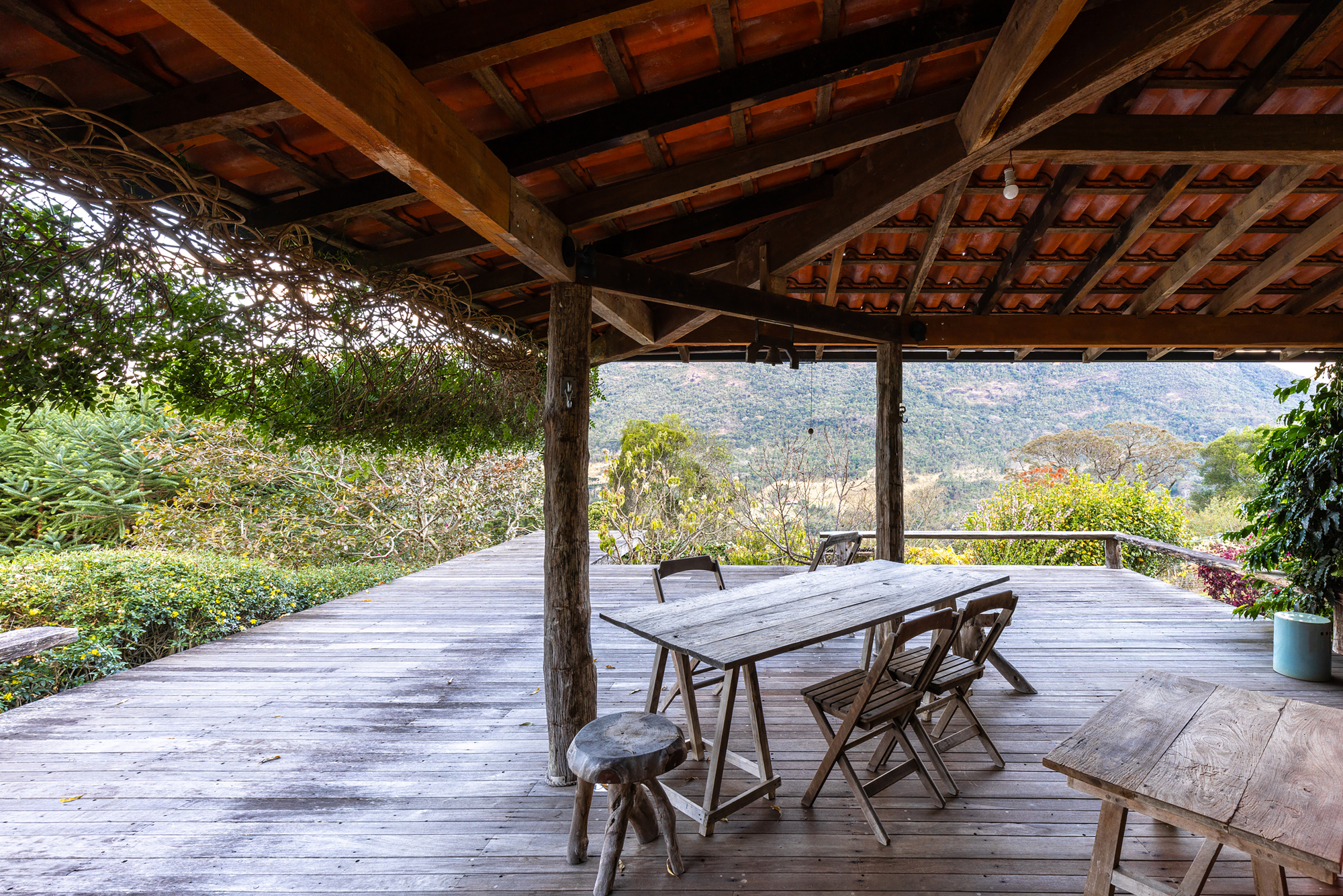 Covered timber deck with trestle table and folding chairs facing forested hills under a clay tile roof