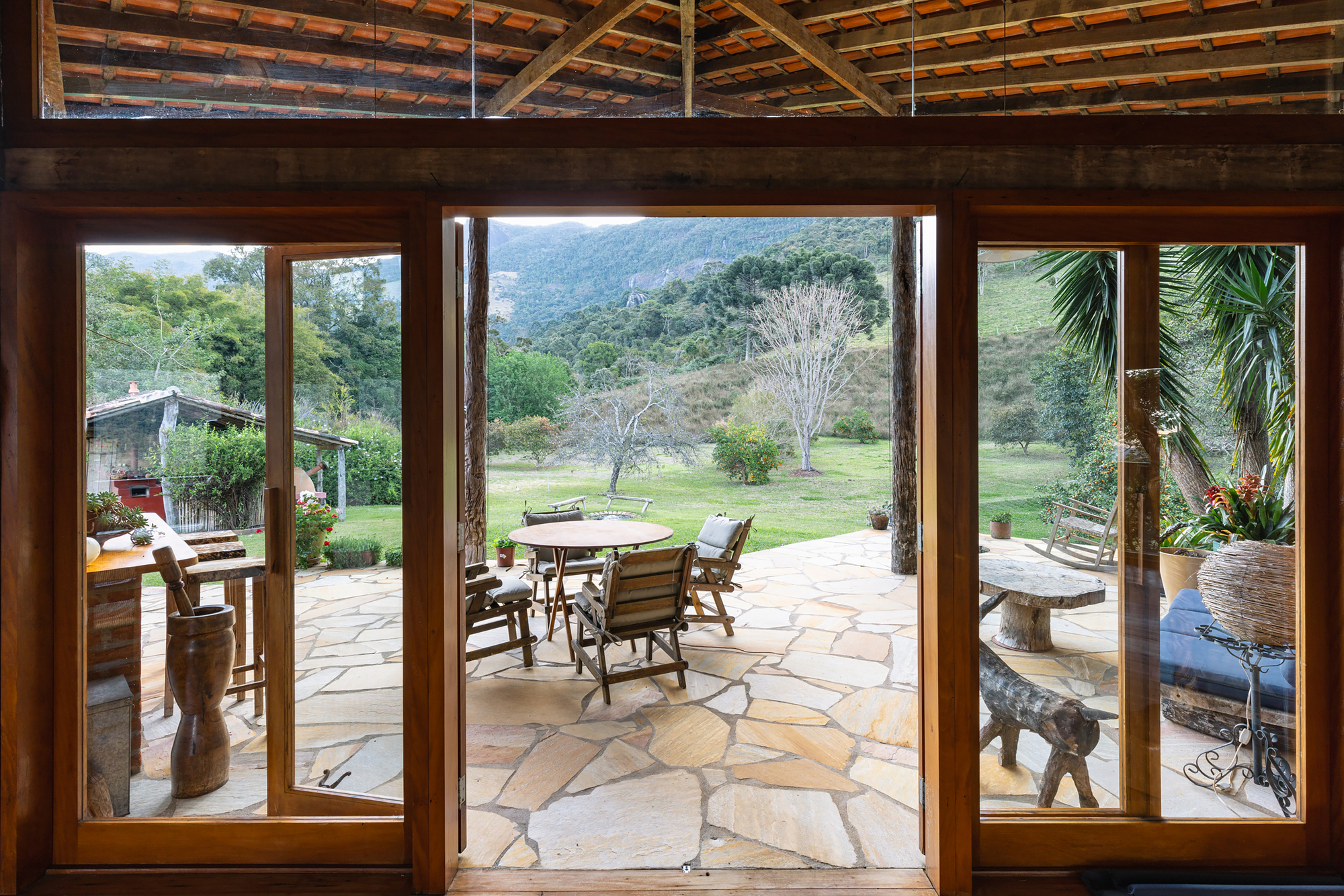 View through open wood-framed glass doors to a flagstone terrace, round table and distant green hills