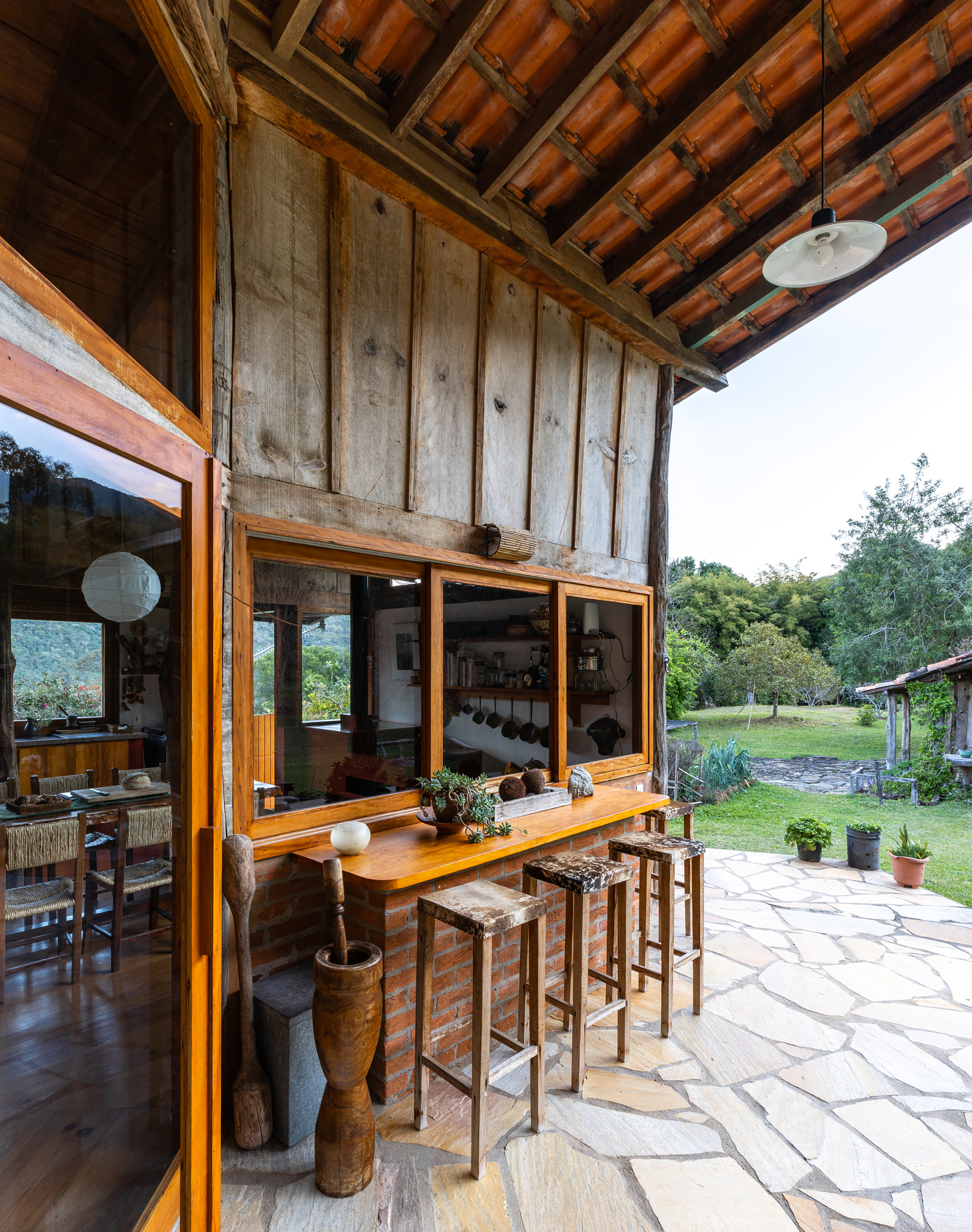 Outdoor kitchen counter with wooden stools beside a brick base and reclaimed plank wall, on a flagstone patio