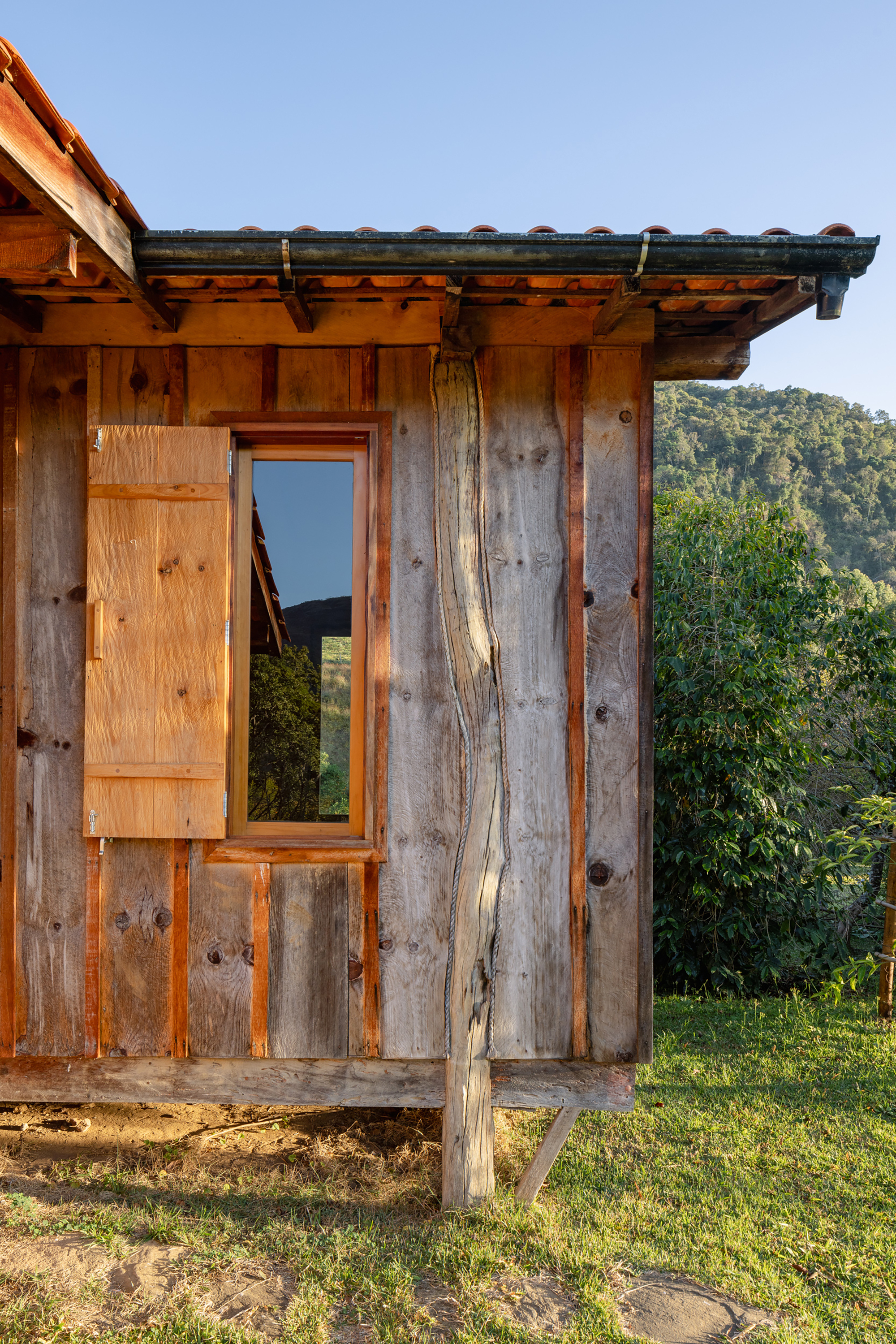 Close-up of a timber wall with an open wooden window shutter, a twisted log post and a tile roof edge