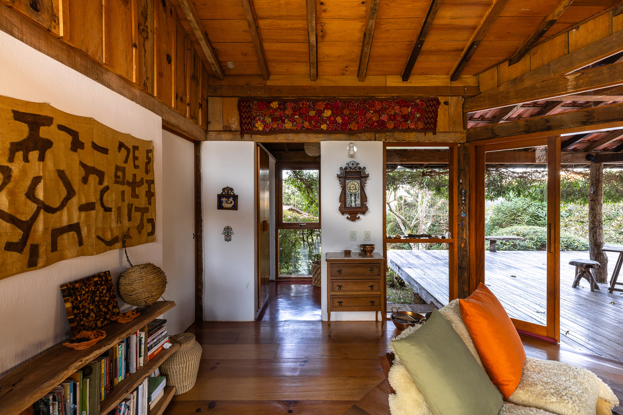 Living area with a woven wall hanging, wooden dresser and sheepskin sofa opening onto a deck through glazed timber doors in warm daylight