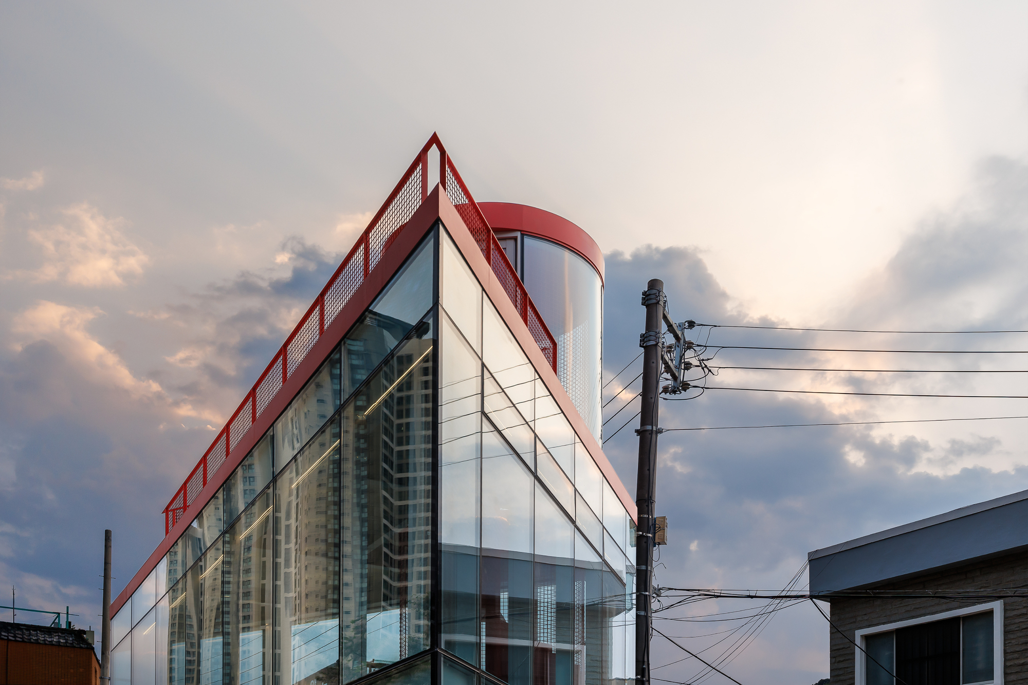 Corner of the glazed volume with red mesh railing and curved stair cap against a pink and grey dusk sky