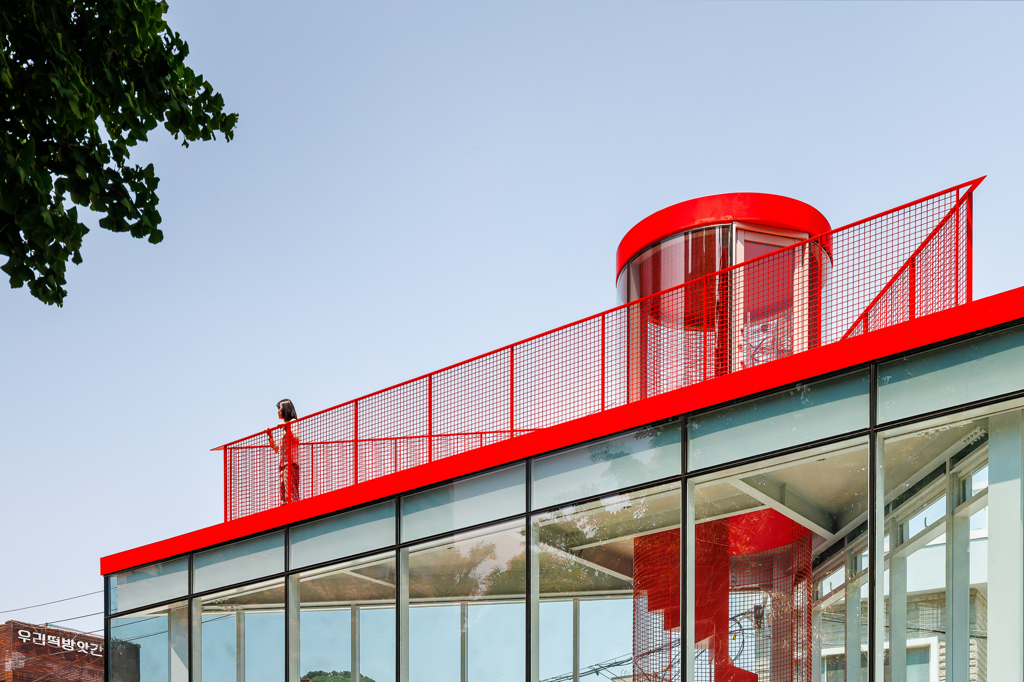 Close-up of the red roof edge, mesh guardrail and cylindrical stair enclosure with a figure standing on the terrace