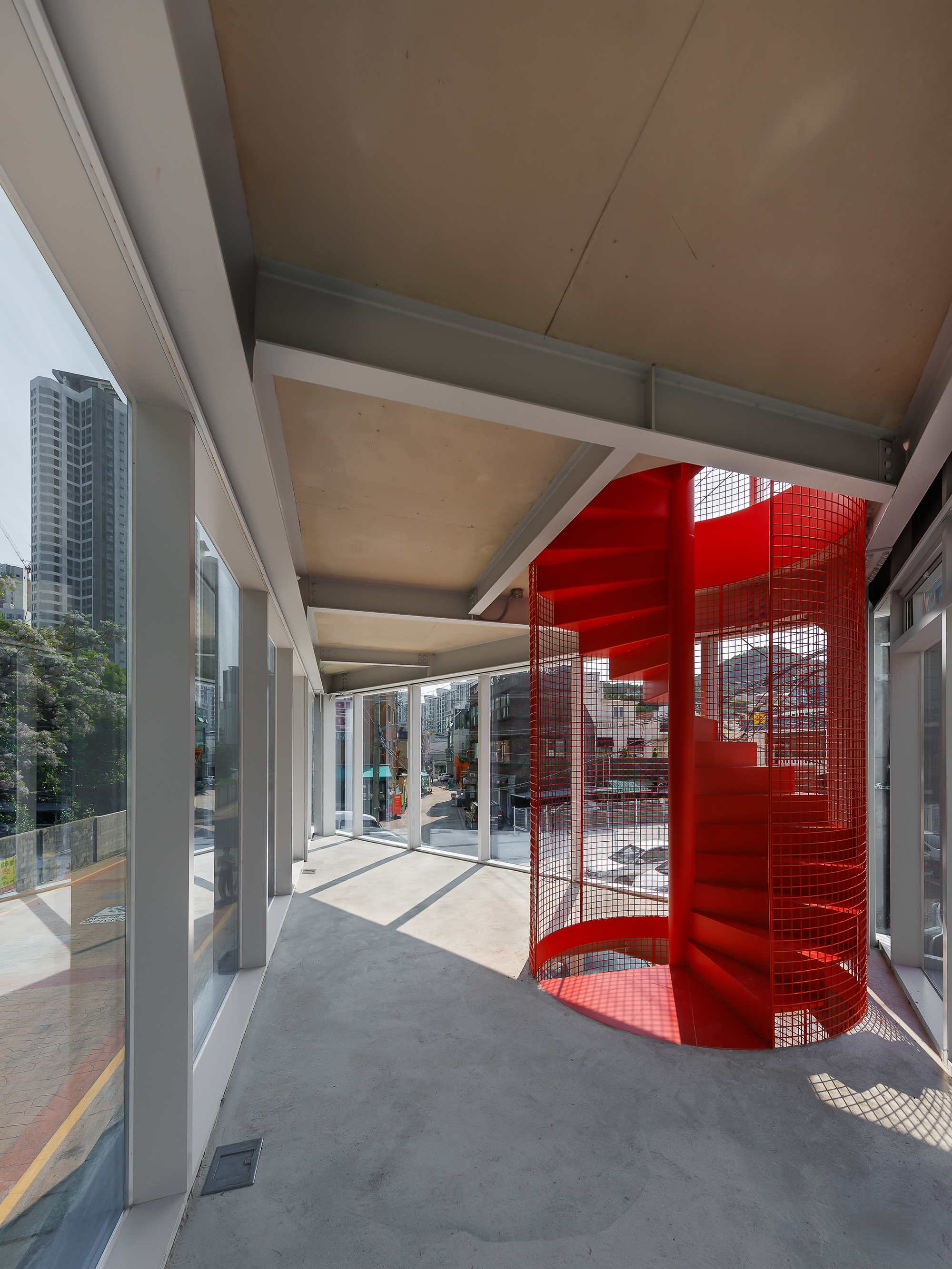 Interior of the upper floor showing the red spiral mesh staircase, exposed steel beams and concrete floor lit by afternoon sun