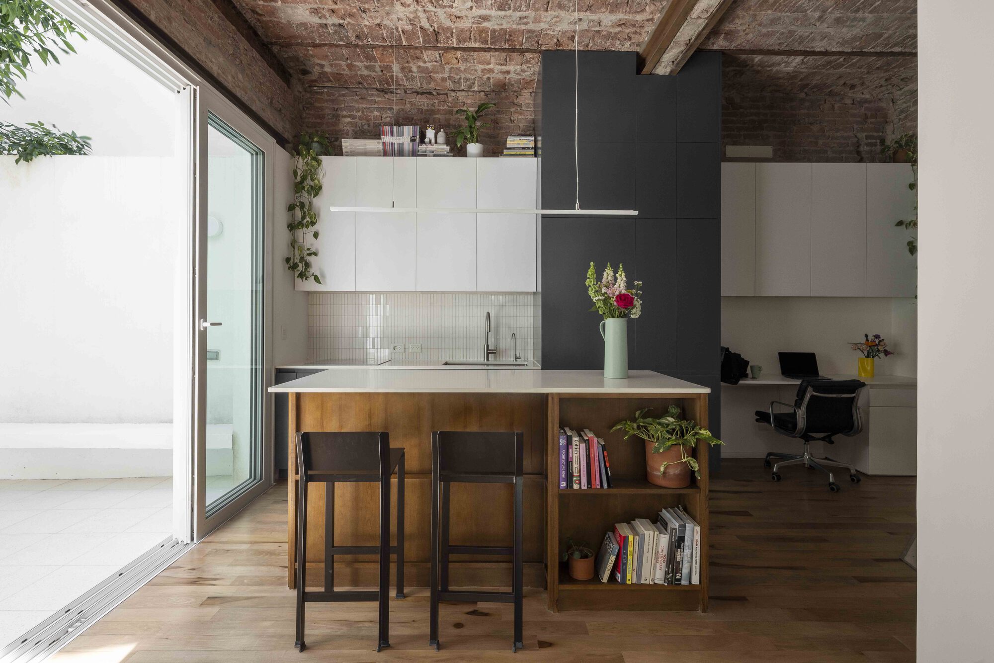 Kitchen island with wood base, open bookshelf and two black stools, facing a sliding glass door open to the patio
