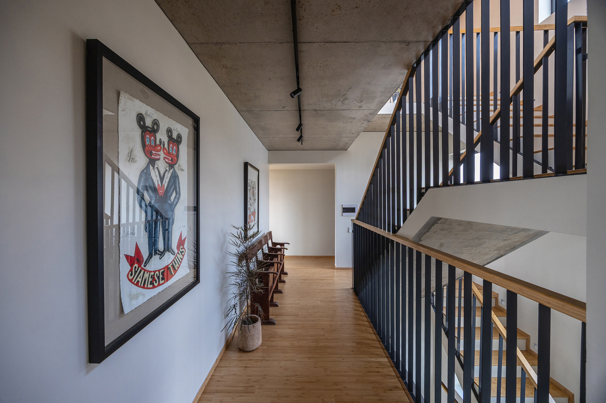 Upper hallway with a framed poster, bamboo floor and black steel balustrade beside a stair, lit by daylight from above