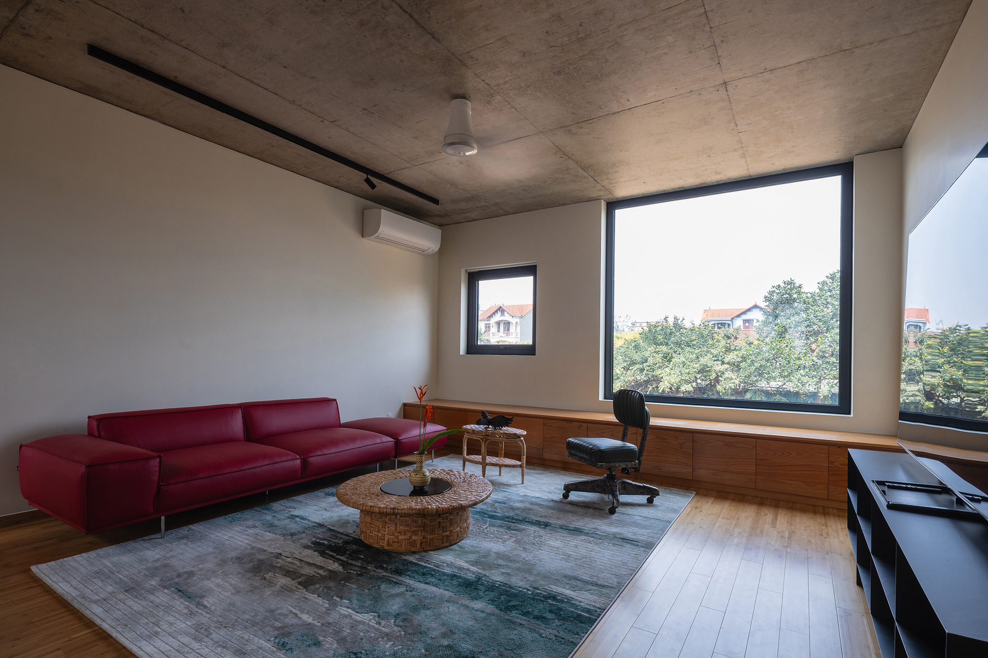 Sitting room with a red leather sofa, wicker coffee table and timber window bench facing a large window onto treetops