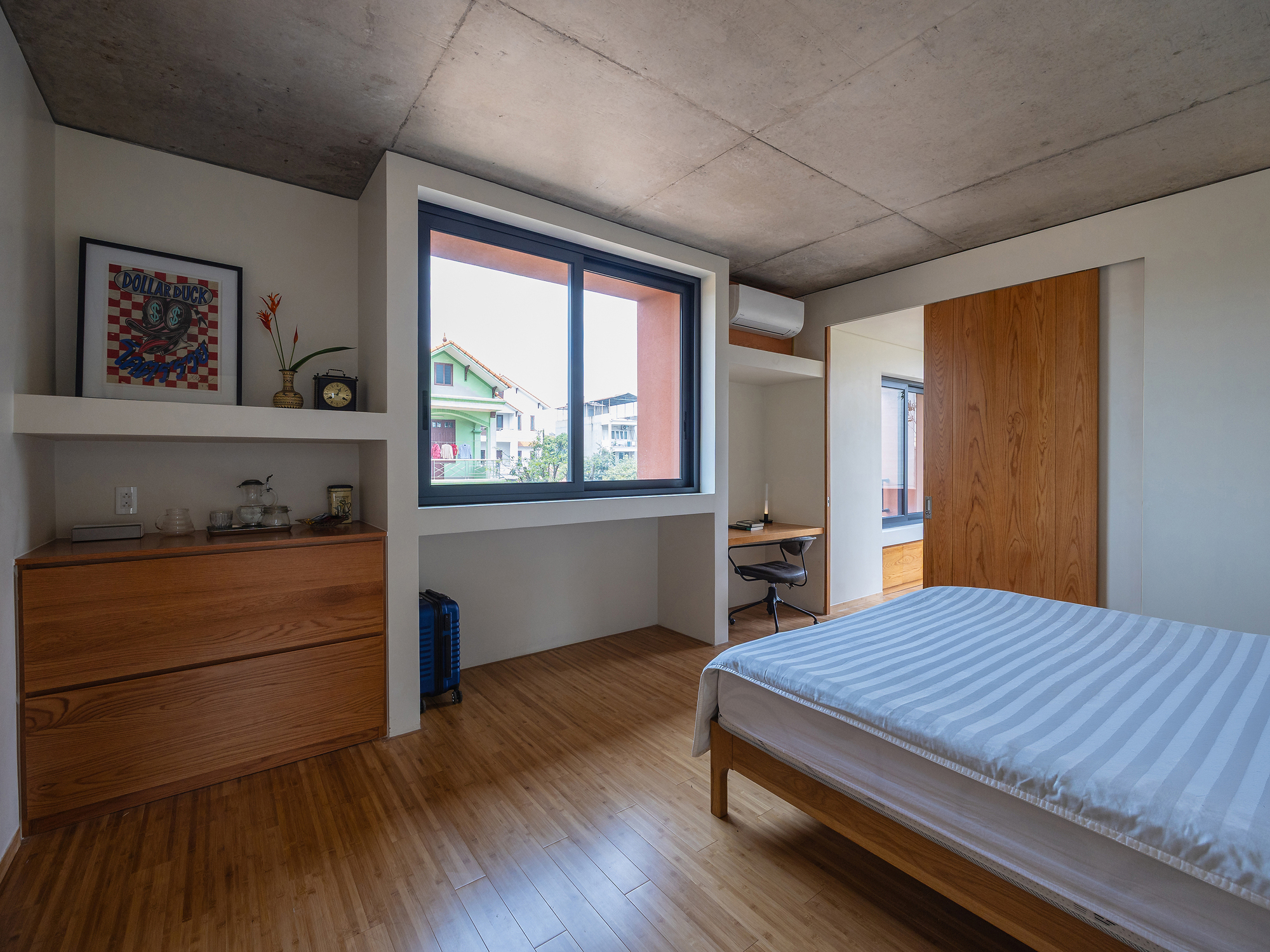 Bedroom with an oak chest of drawers, built-in shelf and desk niche beside a window looking onto neighboring houses