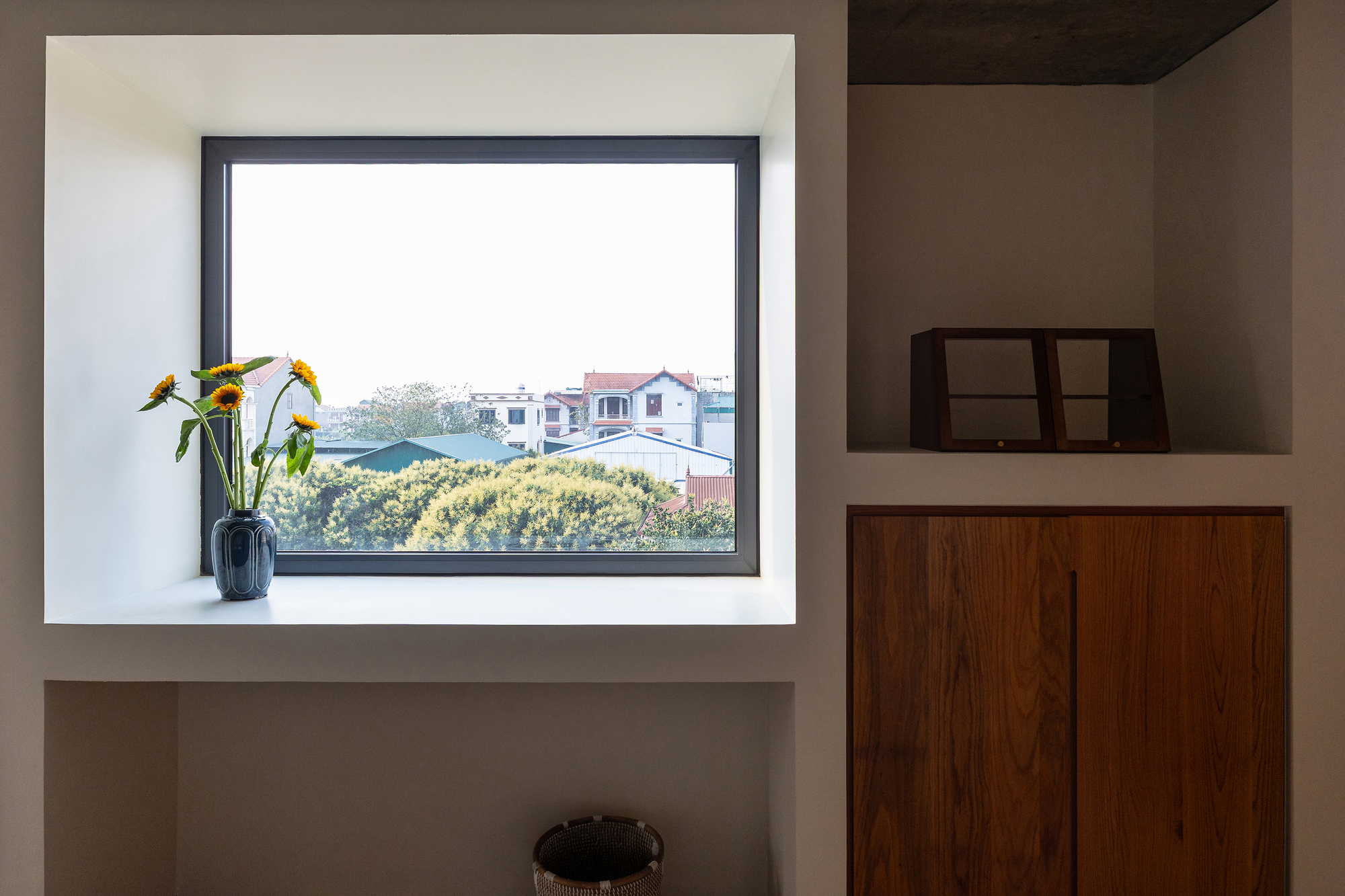 Deep white window recess holding a vase of sunflowers, next to built-in shelves and a walnut cabinet door